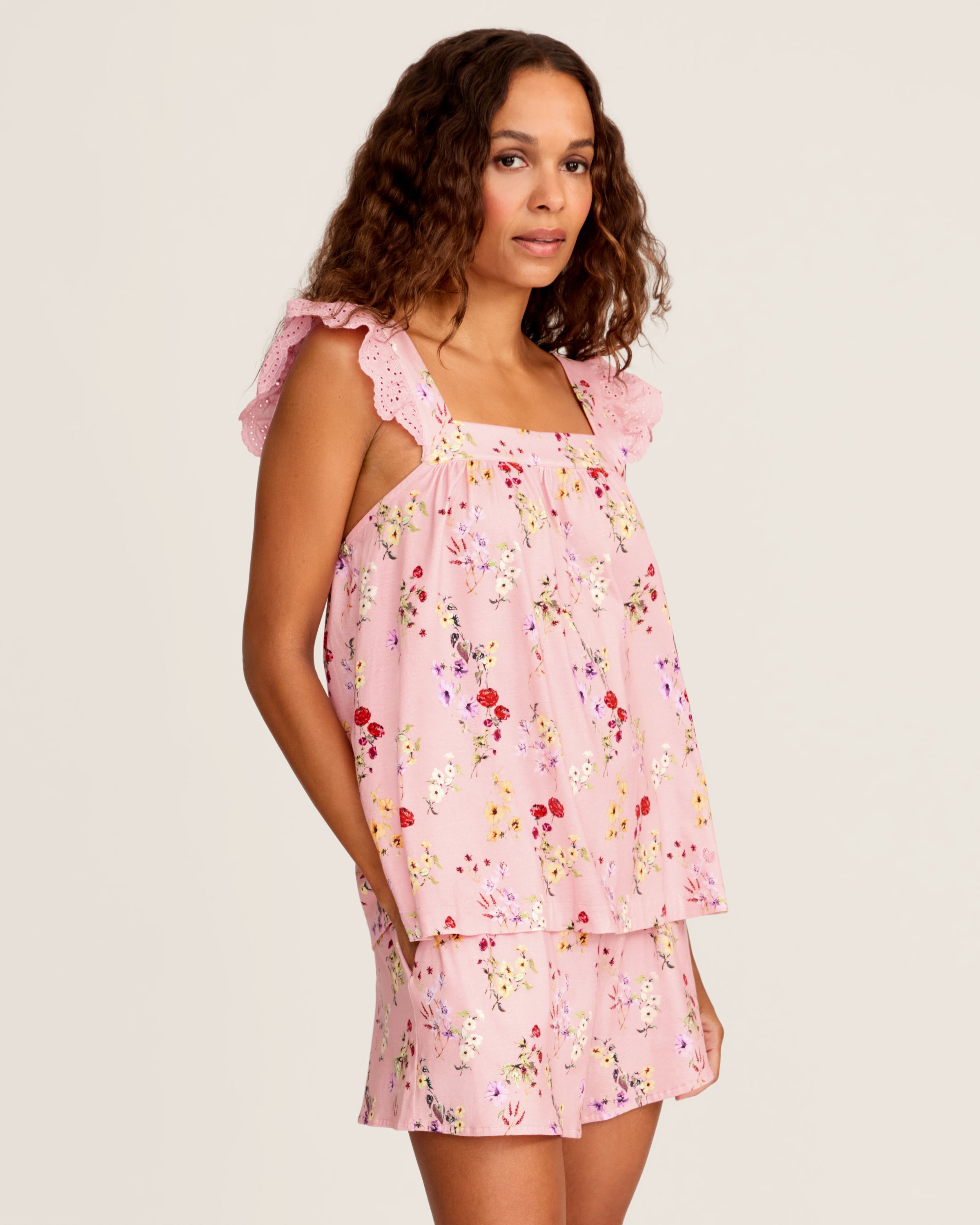 The Women's Pima Clara Short Set in Brilliant Botanical Blush features a matching pink pajama set with a sleeveless top, ruffled straps, and shorts, both adorned with a colorful botanical print.