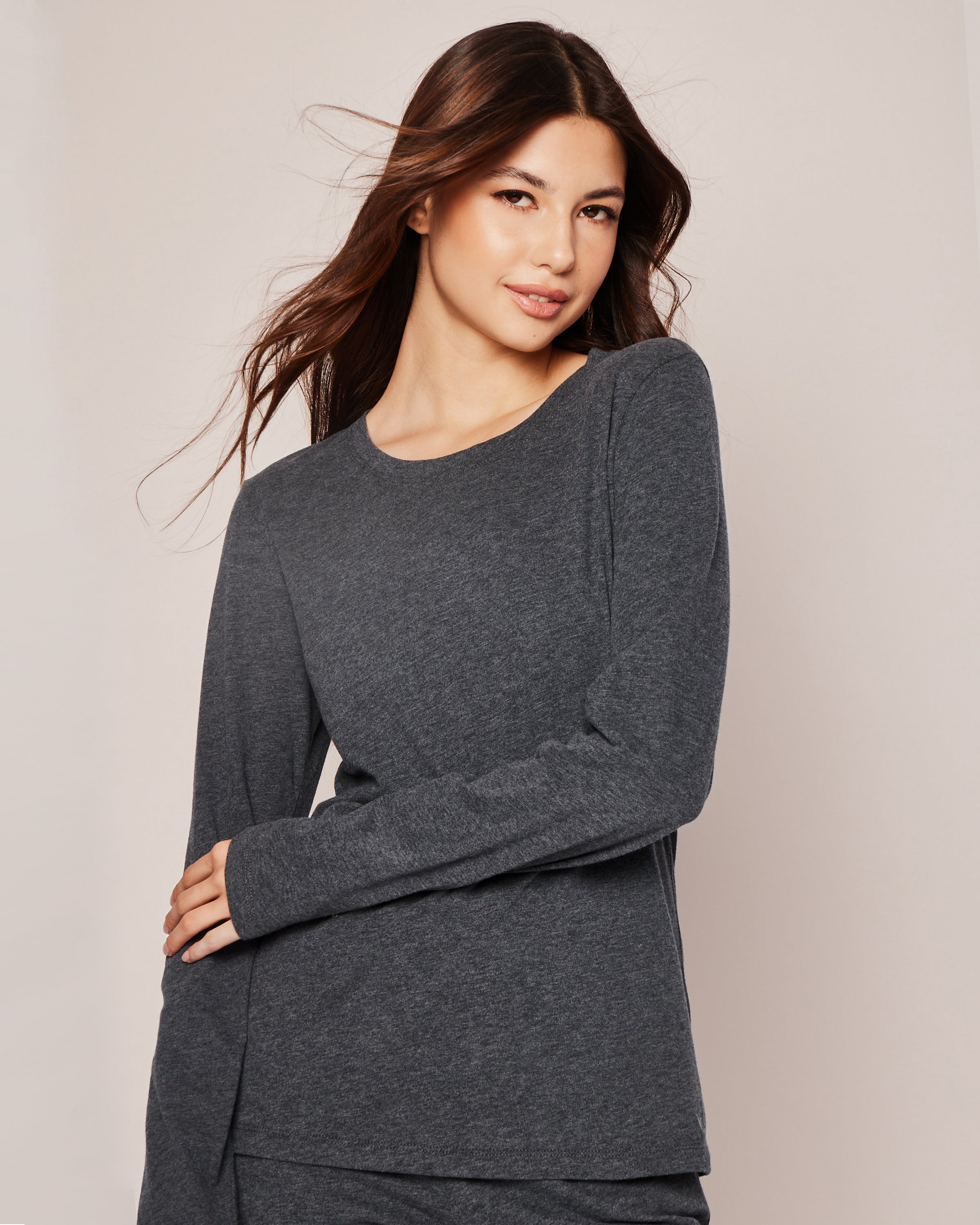 A person with long brown hair poses and smiles in a Womens Pima Long Sleeve Top in Dark Heather Grey by Petite Plume against a light background.