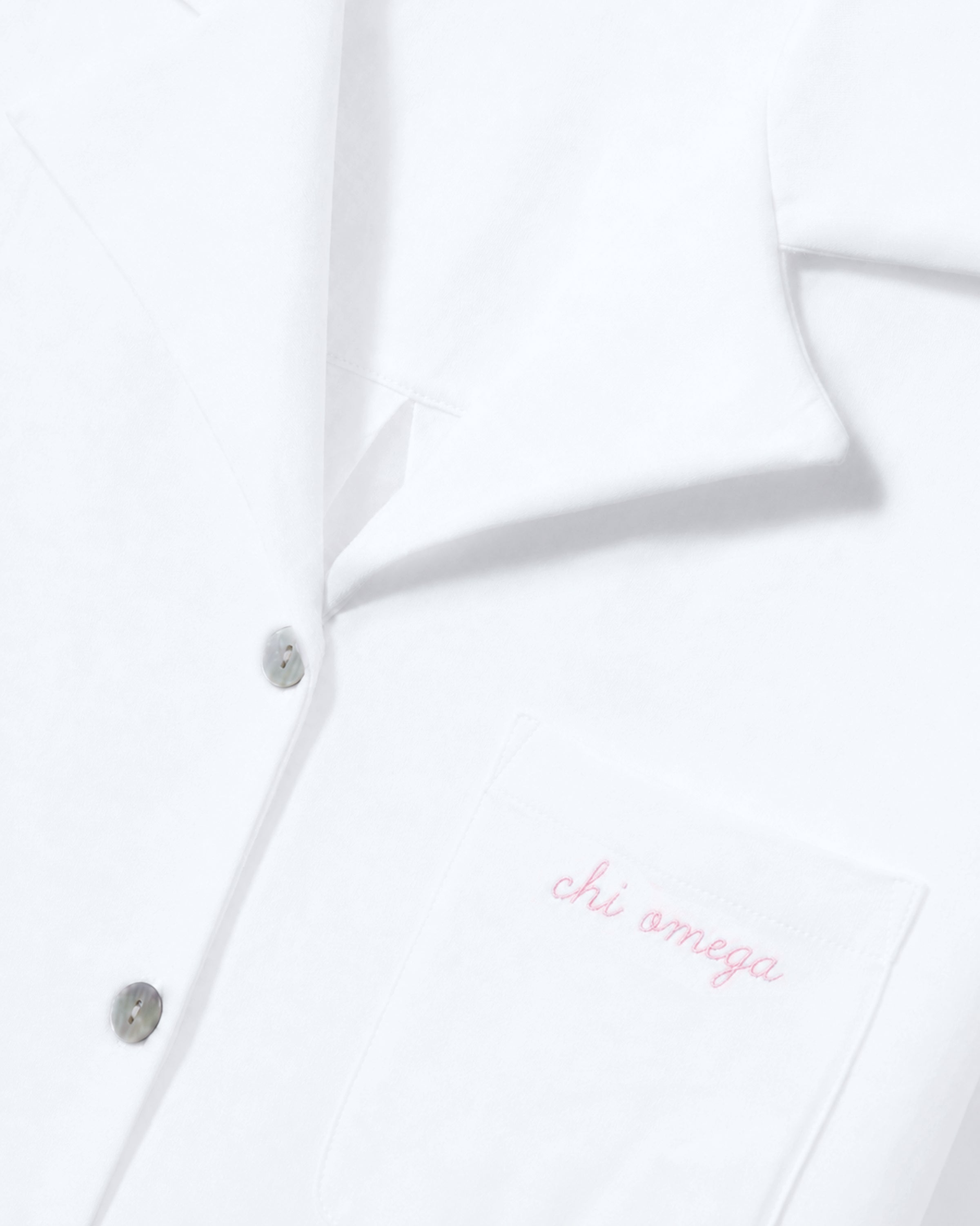 Greek Embroidered Olivia Pima Short Set in White, featuring a button-up shirt with a close-up of the collar and pocket. The pocket is embroidered with “chi omega” in light pink cursive text.