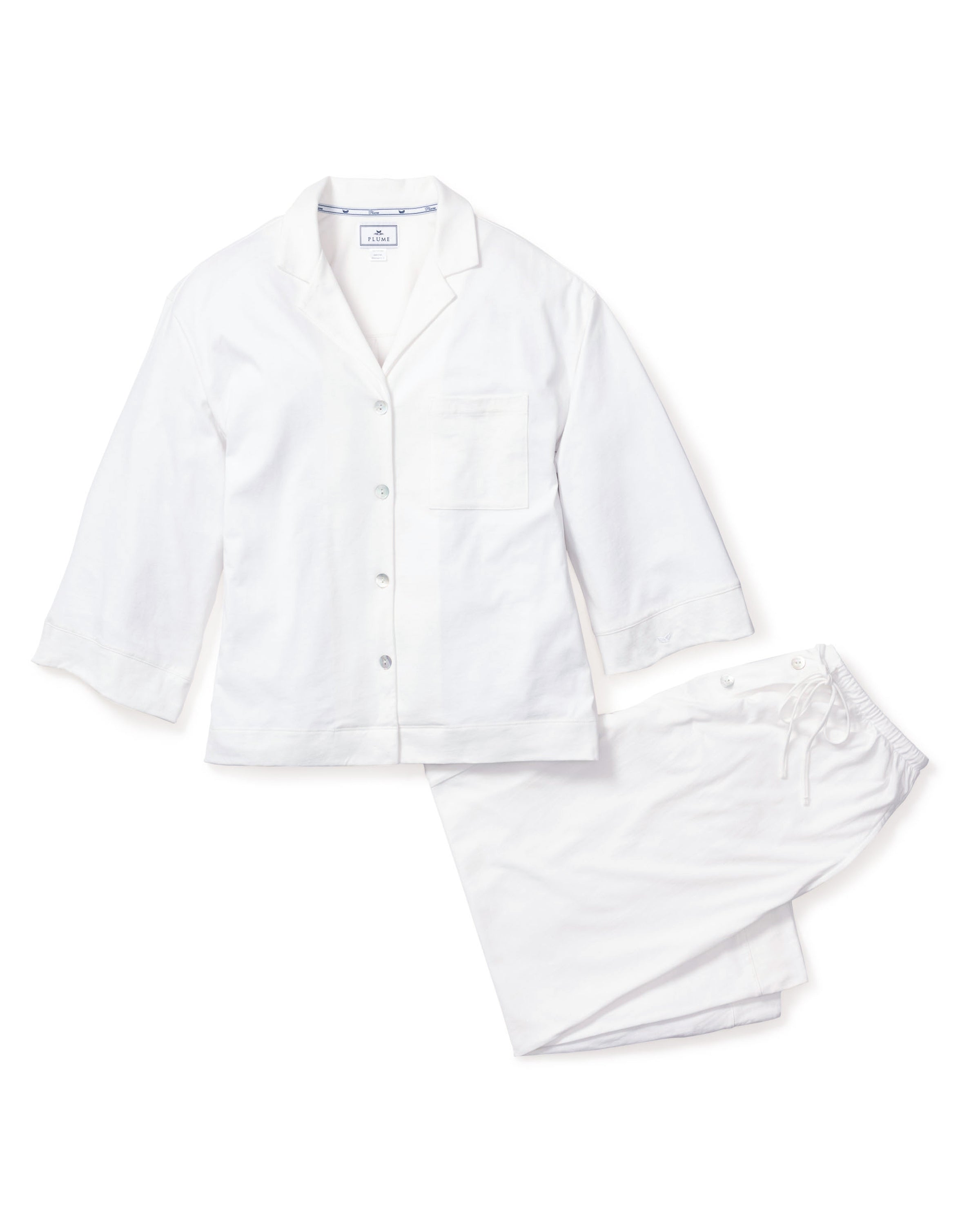 The Olivia Wide Leg Pima Pajama Set in White by Petite Plume, featuring a white long-sleeve button-up top with a breast pocket and matching wide-leg pajama pants, is displayed on a plain white background.