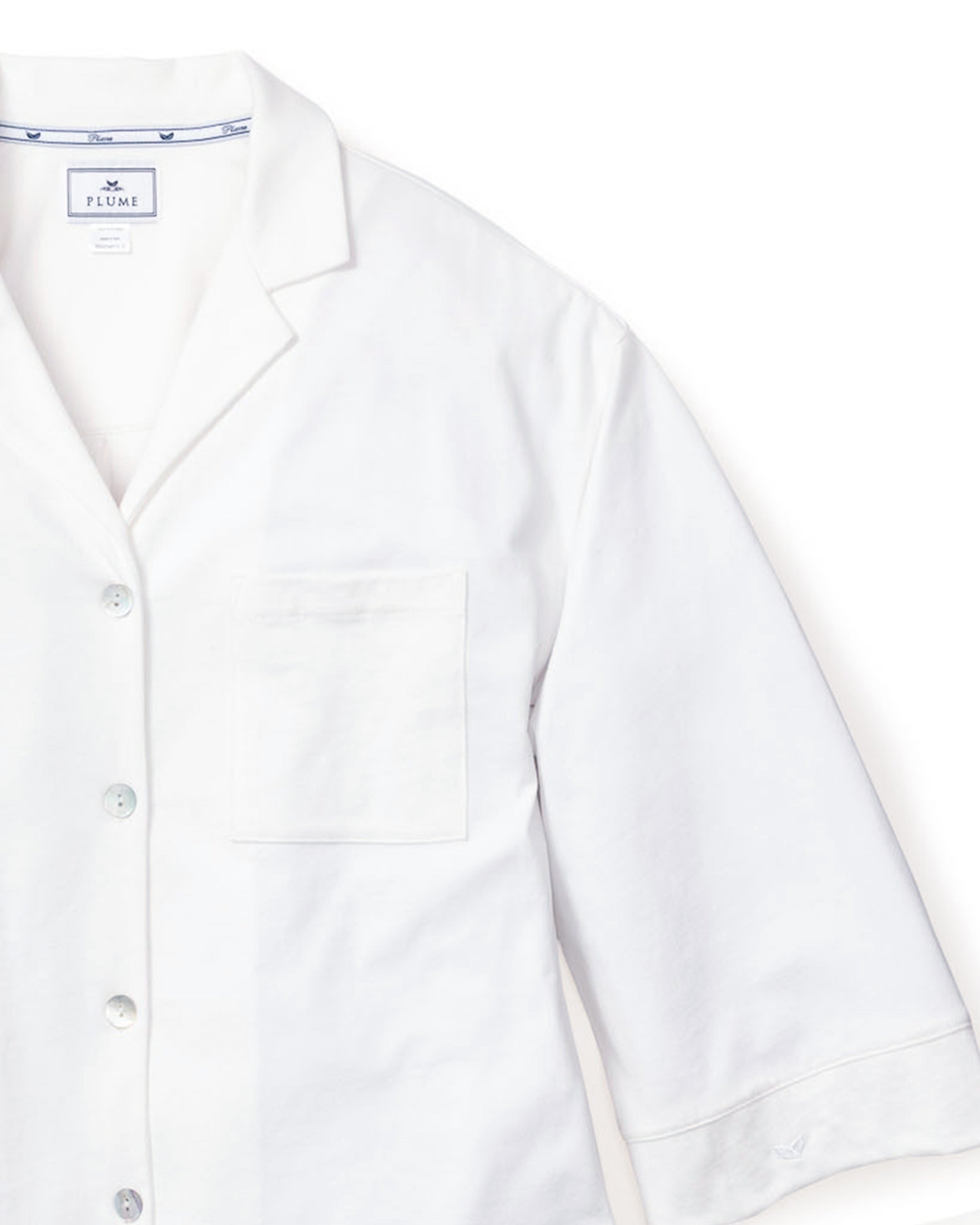 The Olivia Wide Leg Pima Pajama Set in White by Petite Plume features a white button-up shirt with a notched collar, chest pocket, and three-quarter sleeves in Peruvian Pima cotton, paired with wide-leg bottoms for effortless comfort.