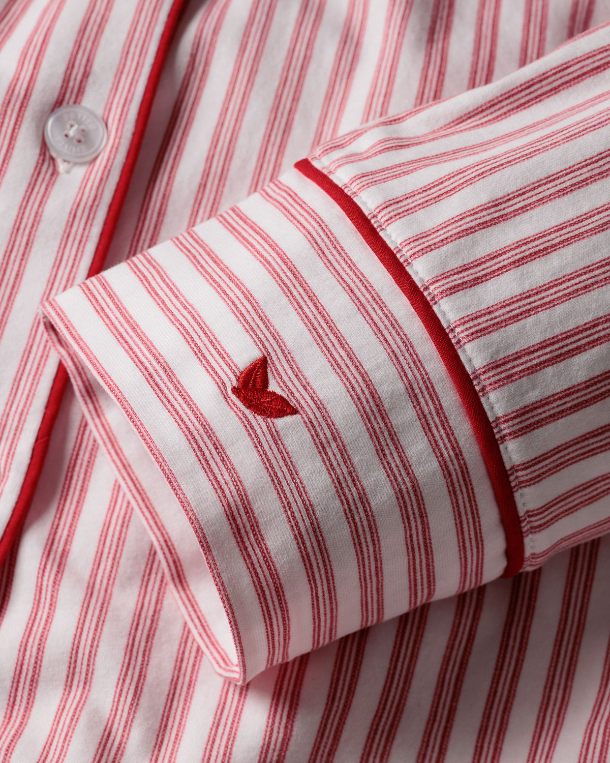 Close-up of the sleeve from the Womens Pima Long Sleeve Short Set in Antique Red Ticking by Petite Plume, featuring a small red embroidered heart and white button. Ideal for luxury sleepwear enthusiasts, its tailored piping adds an exquisite touch. Crafted from Pima cotton.
