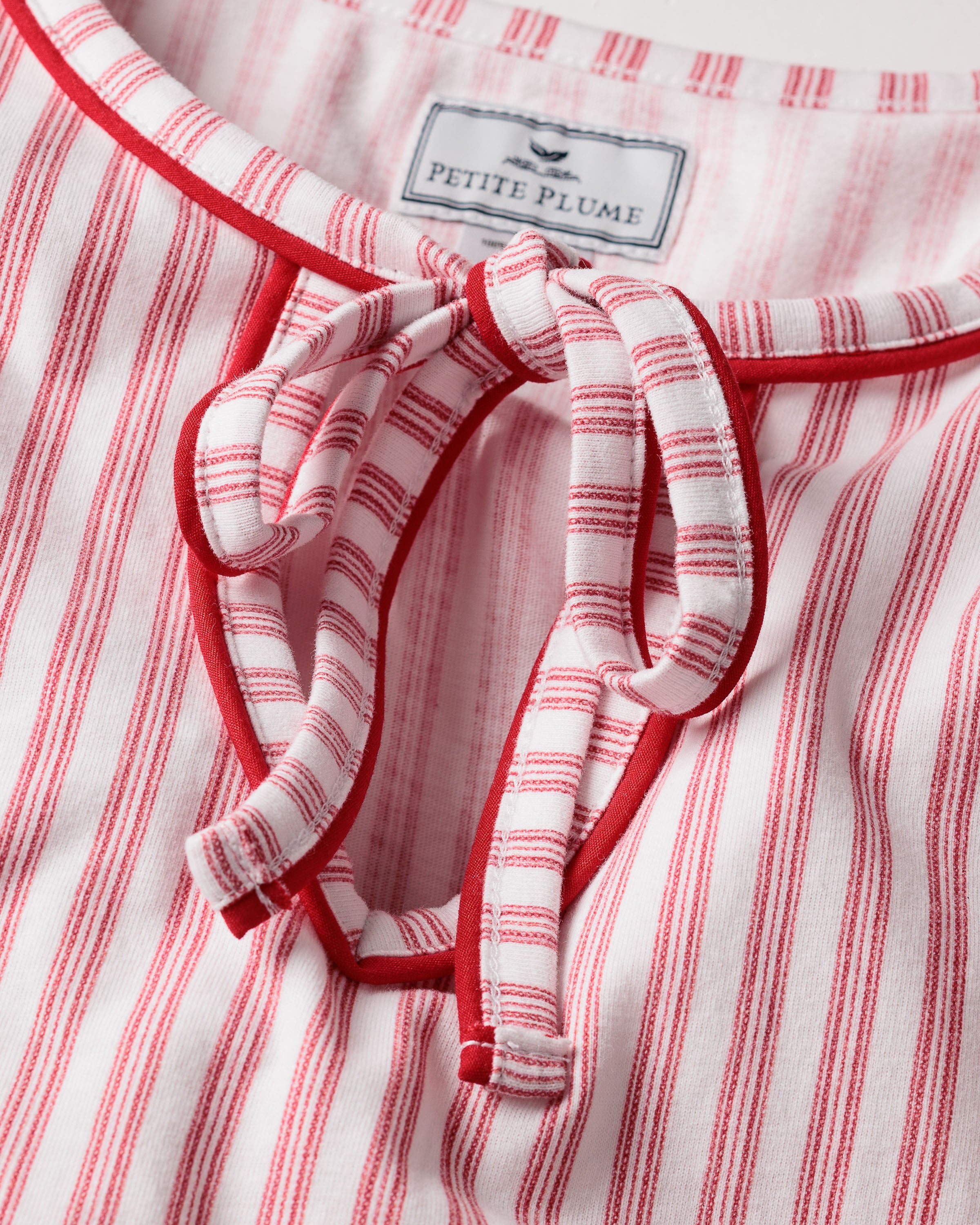 A close-up of the Womens Pima Harlow Nightgown in Antique Red Ticking showcases a red and white striped pattern, made from premium Peruvian Pima cotton. It features a keyhole neckline tied with matching fabric laces, with the Petite Plume label visible on top.