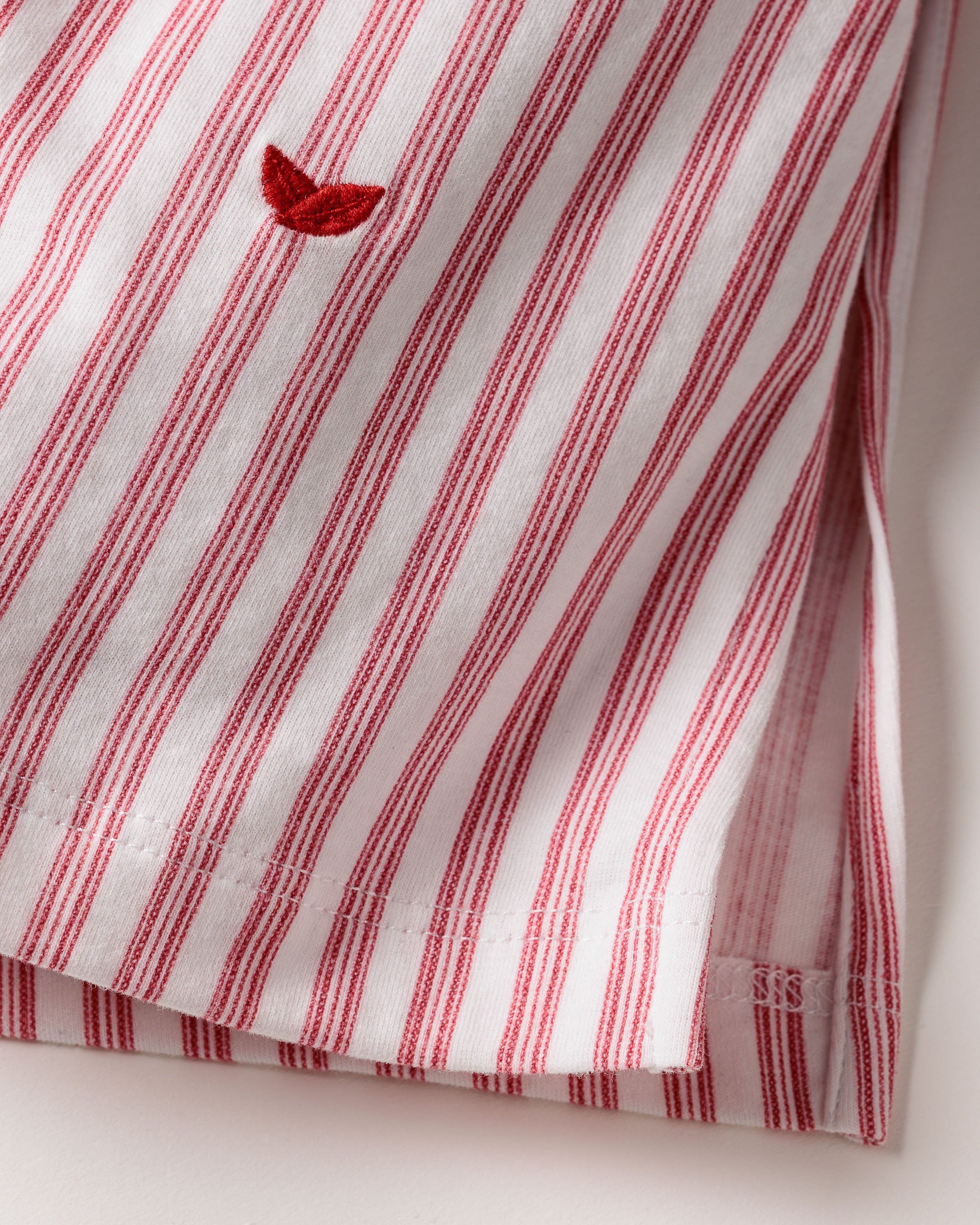 The Womens Pima Harlow Nightgown by Petite Plume, in Antique Red Ticking, features luxurious white Peruvian Pima cotton with red vertical stripes and a small embroidered bird. It has neat seams with visible stitching and a folded corner, displayed on a light surface.