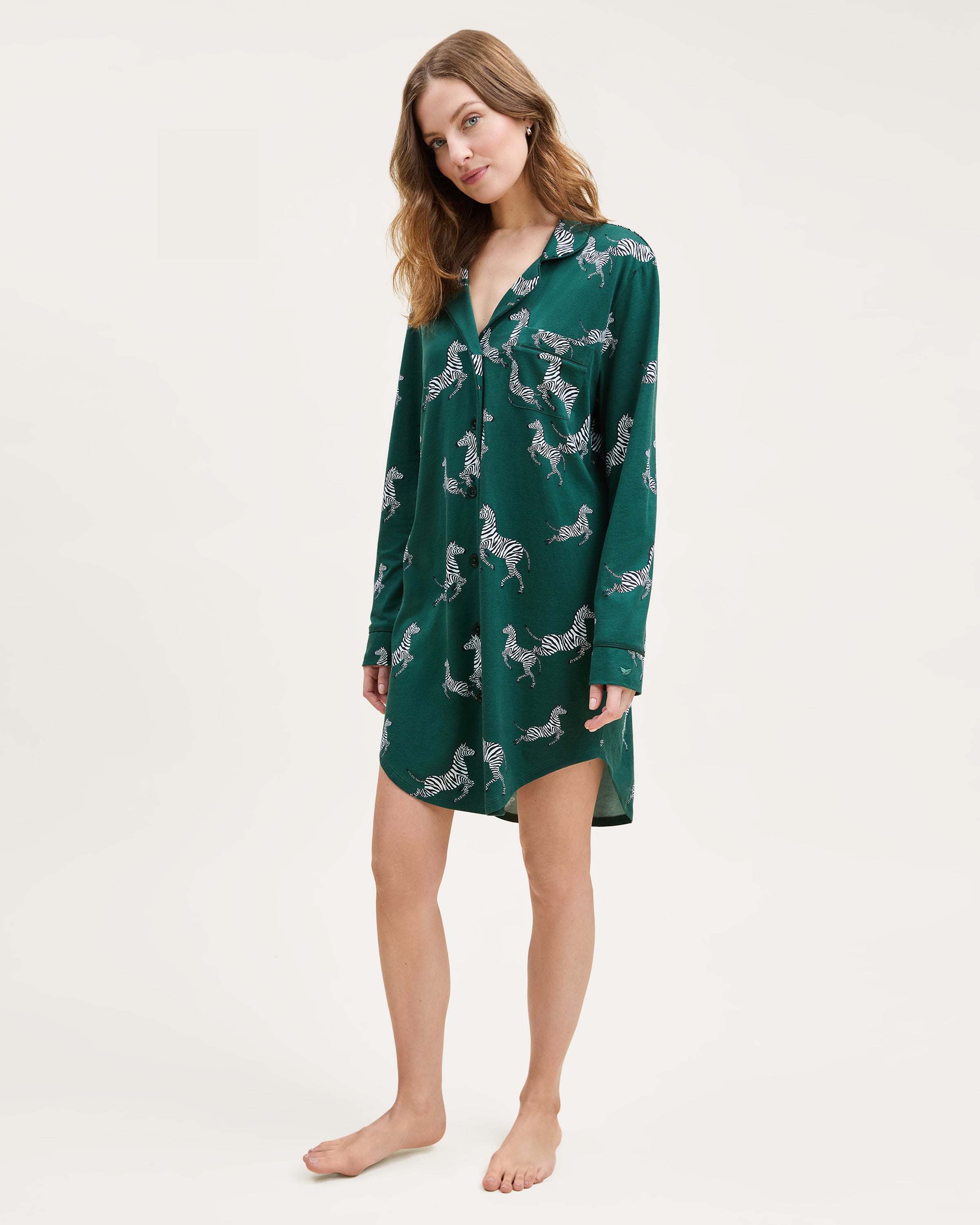 The Women's Pima Nightshirt in Zèbre de Forêt is a long-sleeved, dark green button-up featuring a playful white and black zebra print pattern.