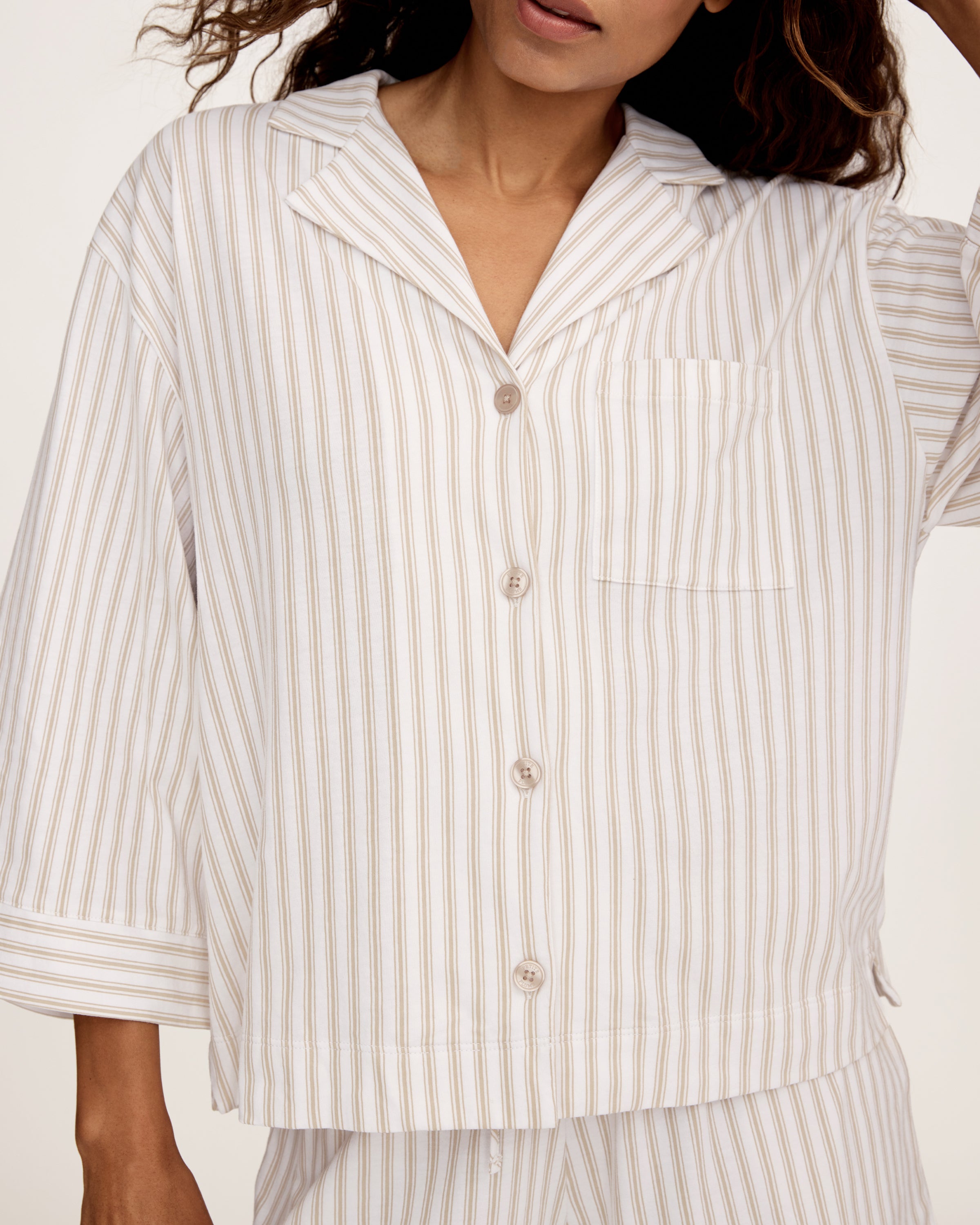 The Olivia Pima Short Set in Camel Ticking features a two-piece pajama set with beige and white vertical stripes, including a button-up, collared long-sleeve shirt with a breast pocket, and matching relaxed-fit drawstring shorts.
