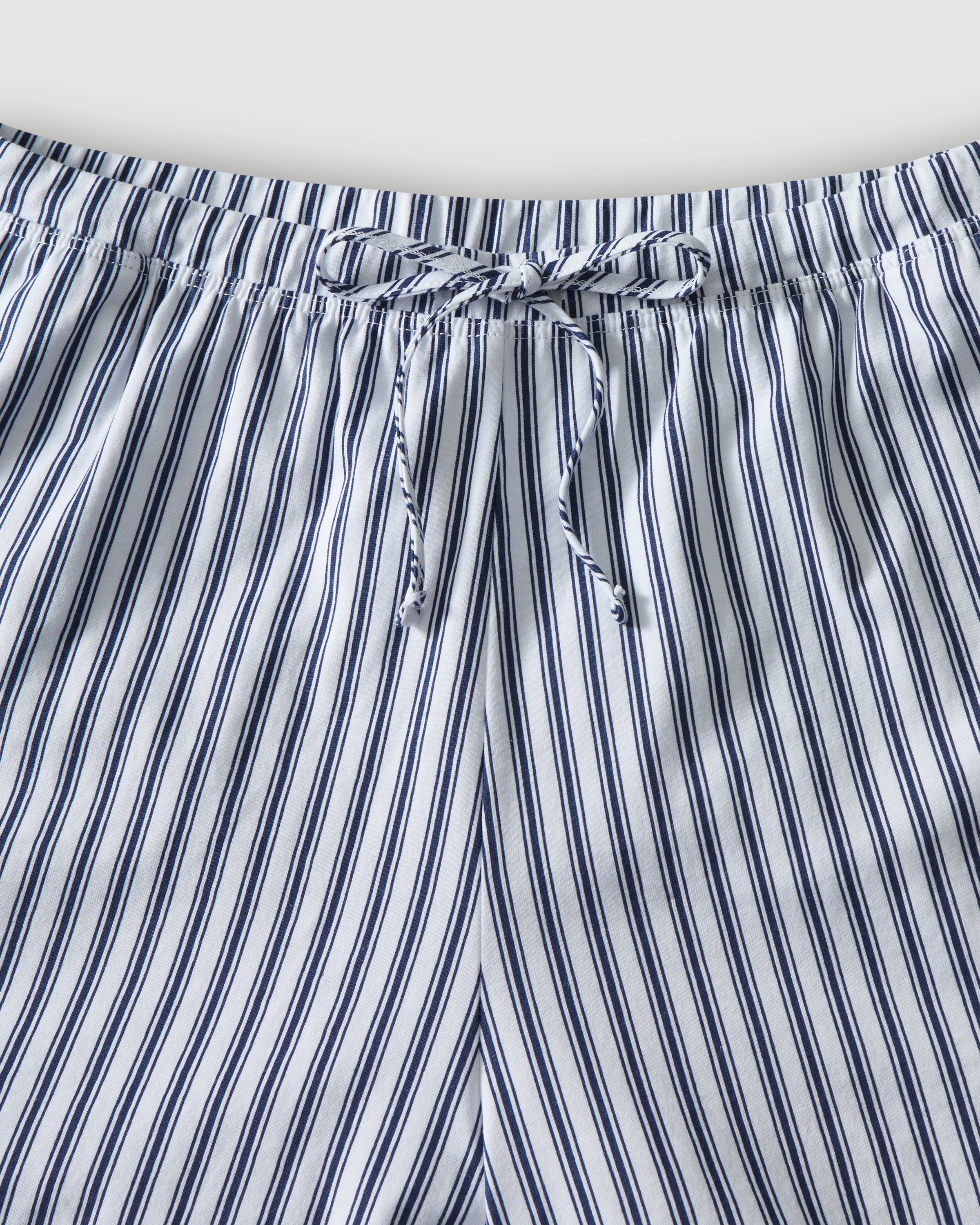 The Olivia Pima Short Set in Navy French Ticking features a matching set of blue and white vertical striped pajamas with a long-sleeve, button-up shirt with chest pocket and drawstring shorts.