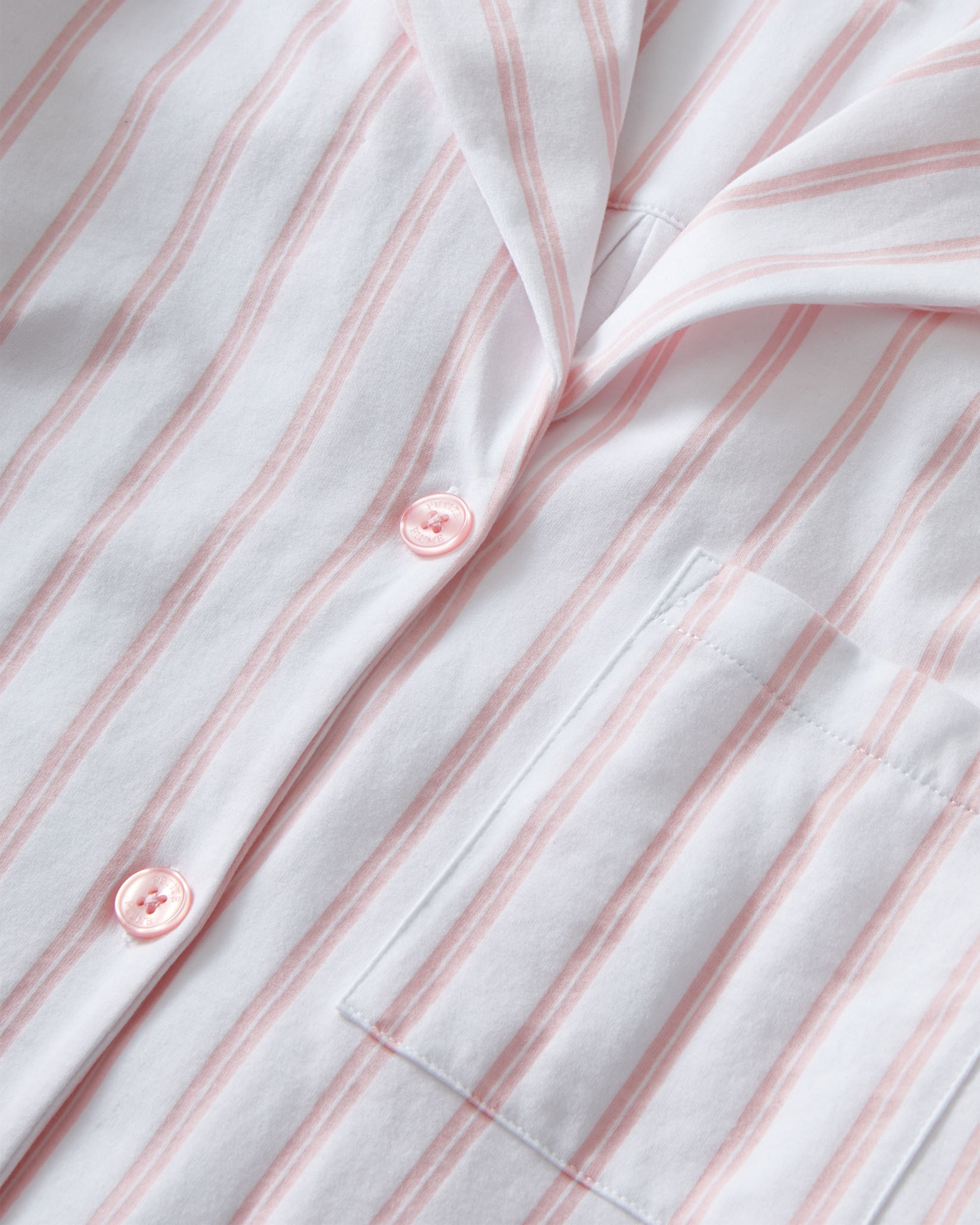 The Olivia Pima Short Set in Pink Stripe features a two-piece pajama set with white and pink vertical stripes, a long-sleeve button-up top with chest pocket, and matching drawstring shorts.