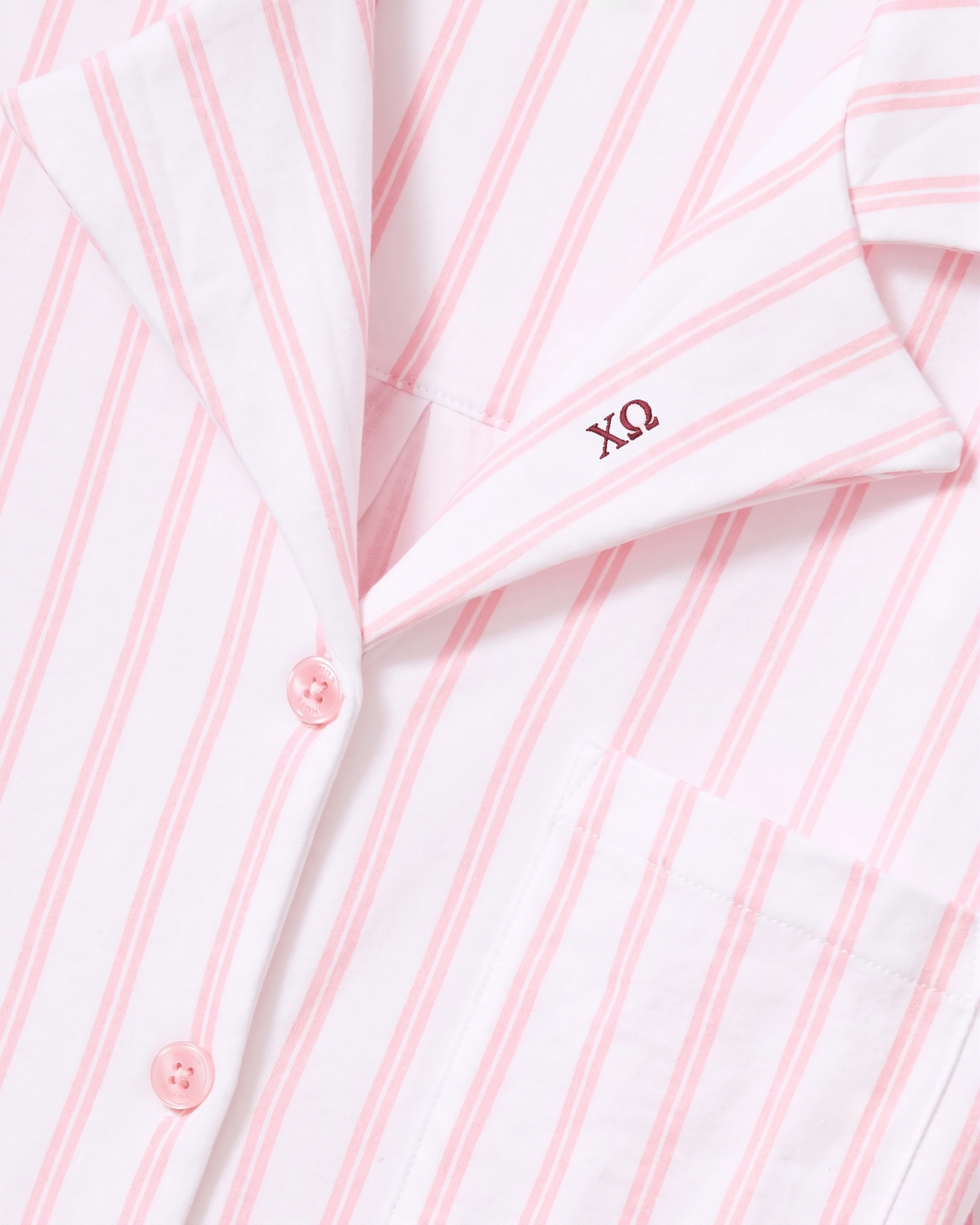 Close-up of the Greek Embroidered Olivia Pima Short Set in Pink Stripe, featuring a white pajama shirt with pink vertical stripes, pink buttons, a pocket, and dark pink Greek letters ΧΩ embroidered on the collar.
