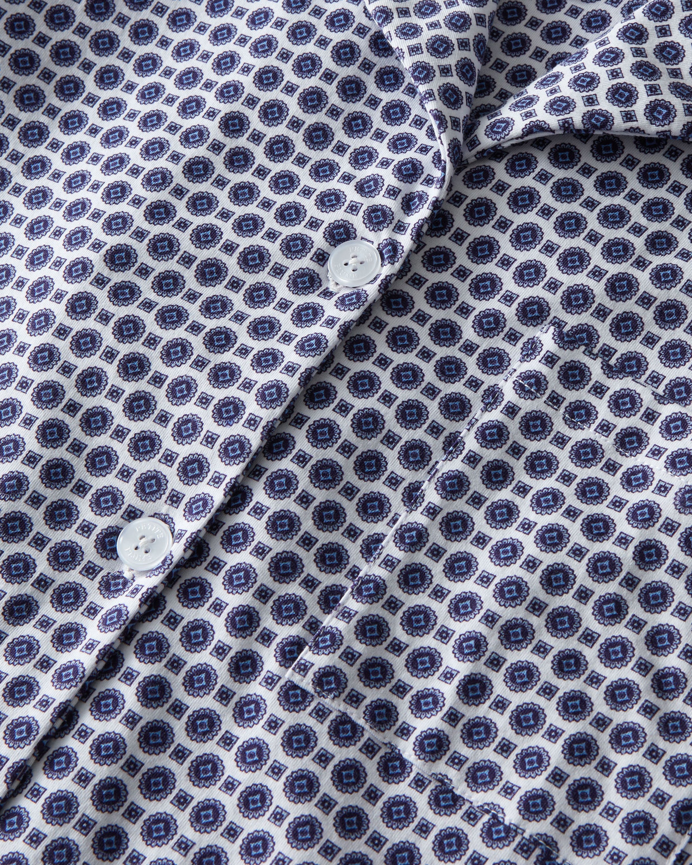 The Olivia Pima Short Set in Navy Foulard features a two-piece pajama set with a blue and white geometric pattern, including a button-up short-sleeve collared shirt and matching shorts.