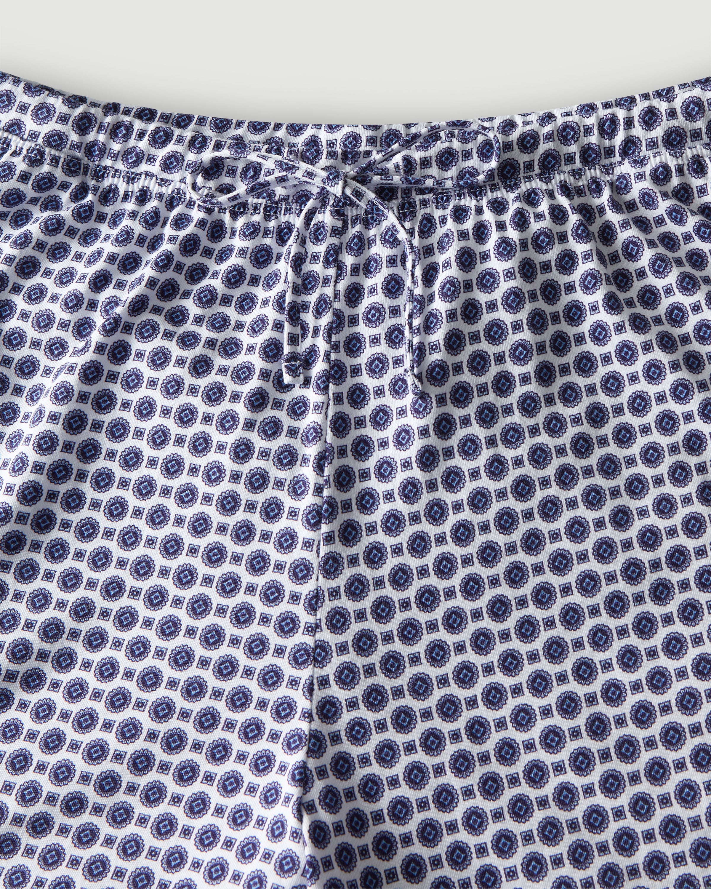 The Olivia Pima Short Set in Navy Foulard features a two-piece pajama set with a blue and white geometric pattern, including a button-up short-sleeve collared shirt and matching shorts.