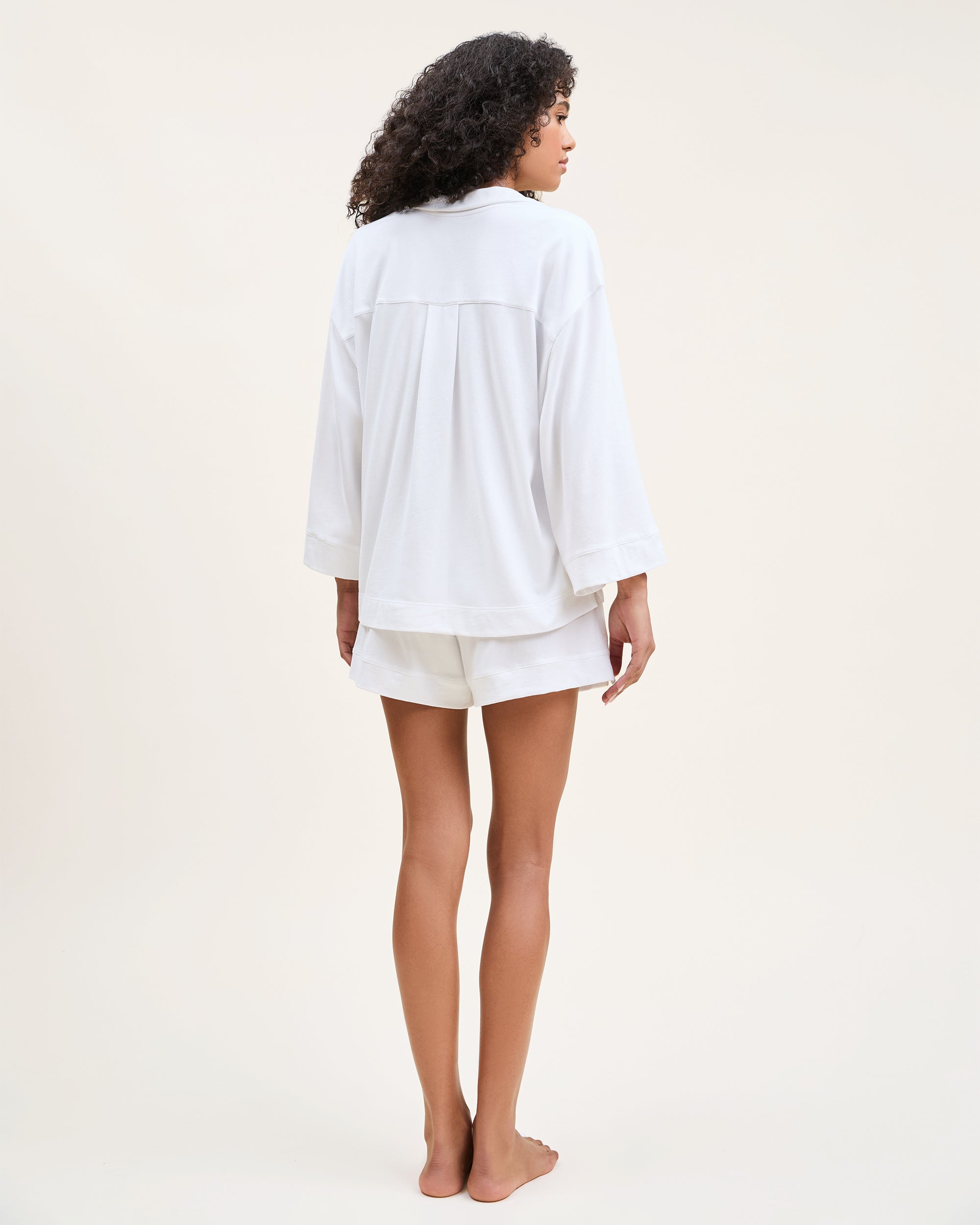 The Olivia Pima Short Set in White features a matching pajama set with a button-up, collared shirt with a chest pocket and three-quarter sleeves, paired with elastic waist drawstring shorts.