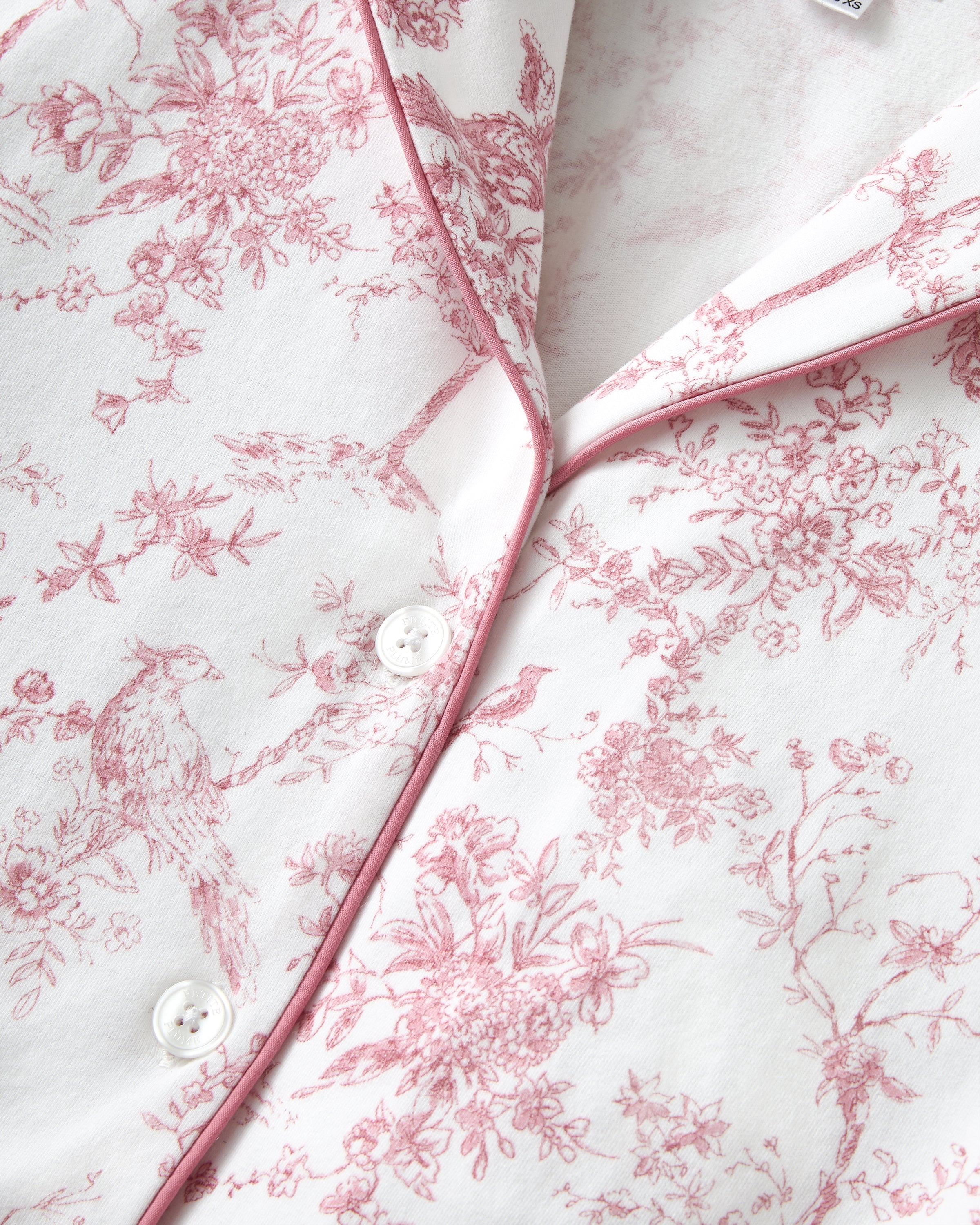 The Margaux Pima Pajama Set in Pink Timeless Toile features long sleeves, soft white fabric with a pink floral toile pattern, and pink piping along the edges and collar.