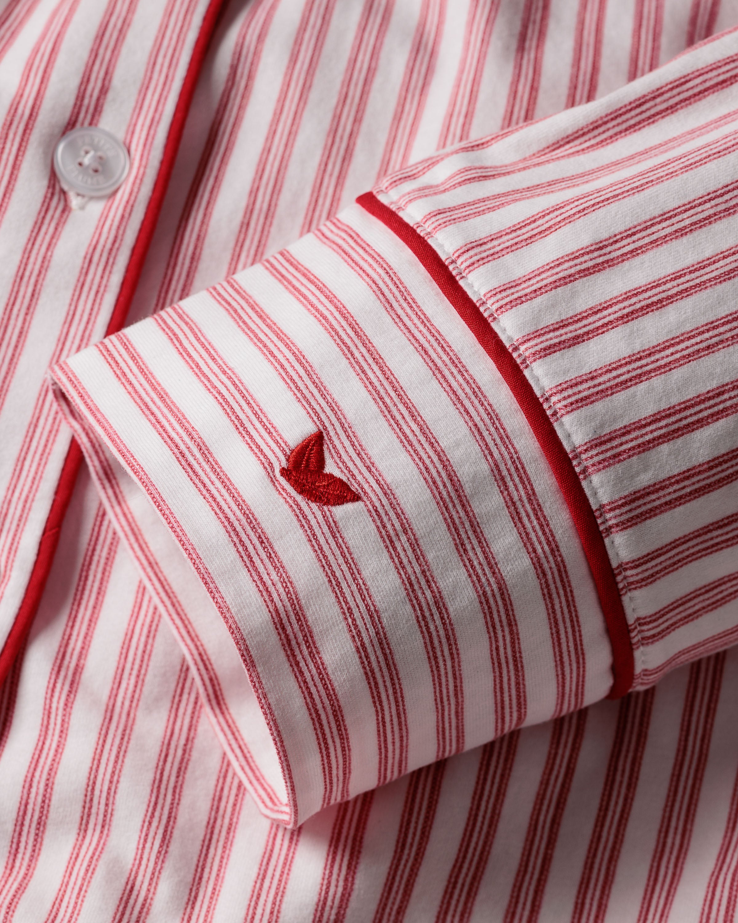 Close-up of Petite Plumes Womens Pima Pajama Set in Antique Red Ticking. Featuring luxurious red and white stripes, a Peruvian Pima cotton sleeve with a small embroidered heart above the cuff, white buttons, and elegant red piping on the cuff.