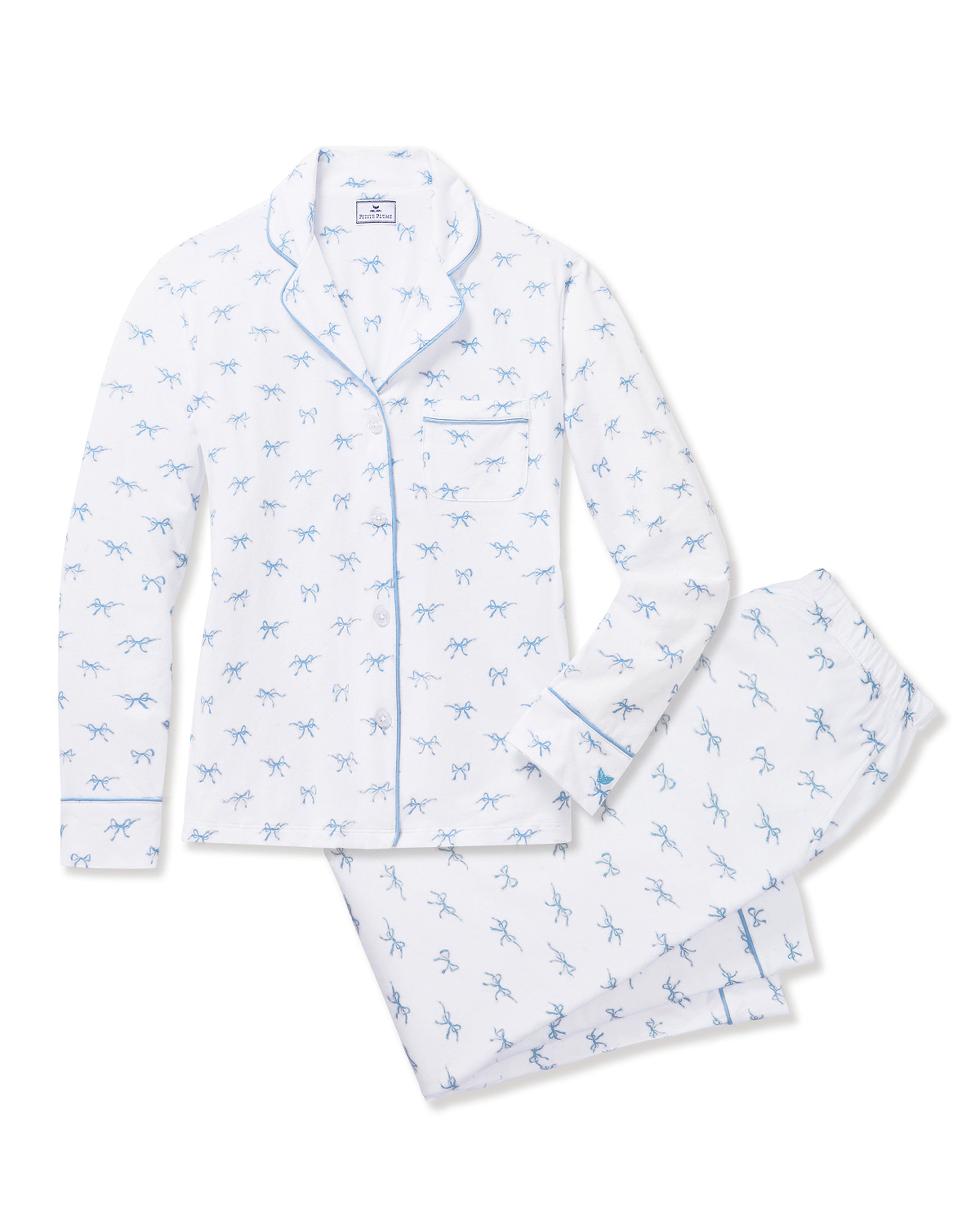 The Women's Pima Pajama Set in Something Blue Bows is a white set with blue piping, including a collared button-up top with chest pocket and matching pants. Both feature a repeating blue print of small bows.