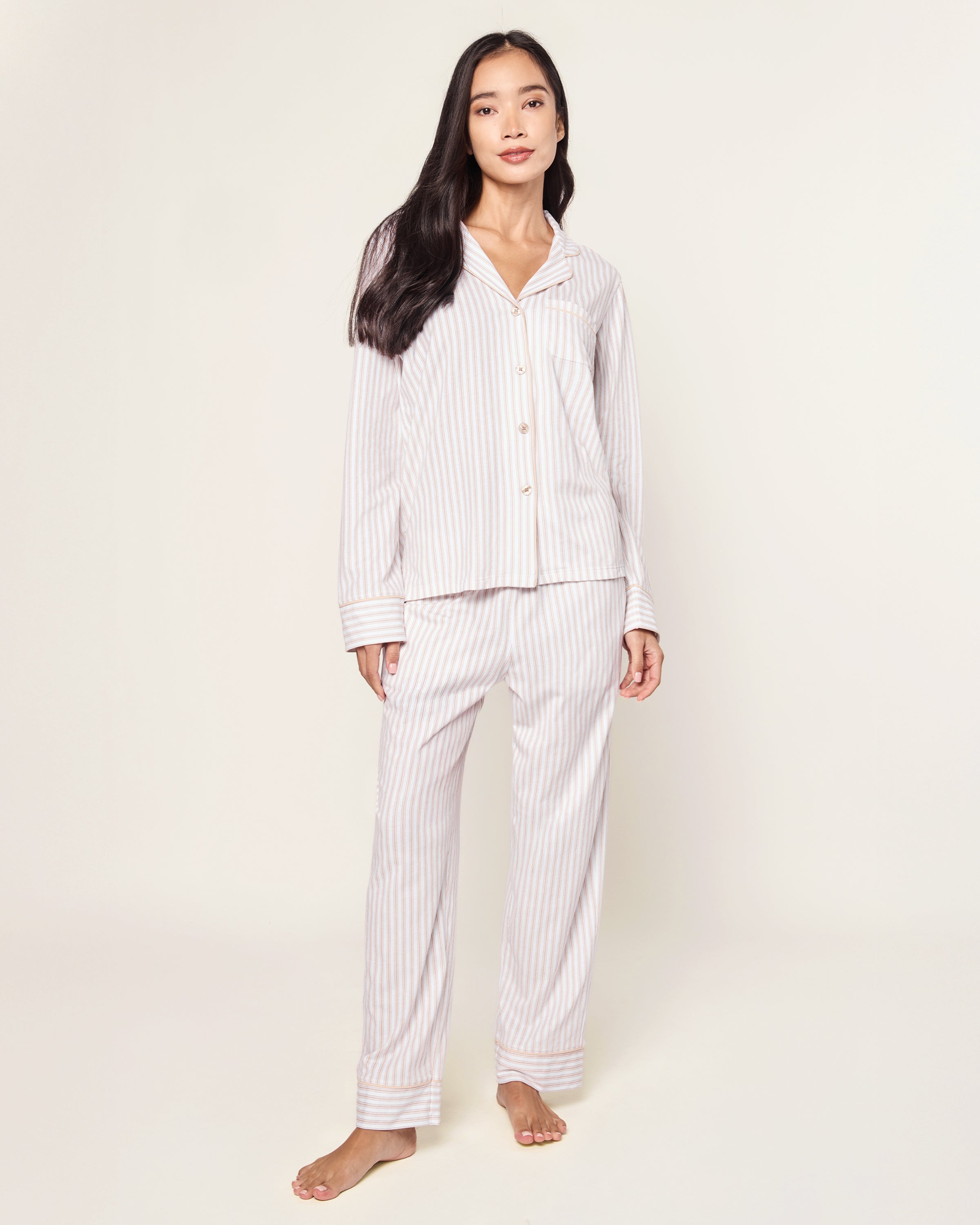 The Women's Pima Pajama Set in Camel Ticking features beige and white vertical stripes, including a long-sleeve button-up top with a chest pocket and matching elastic-waist pants, shown laid flat on a white background.