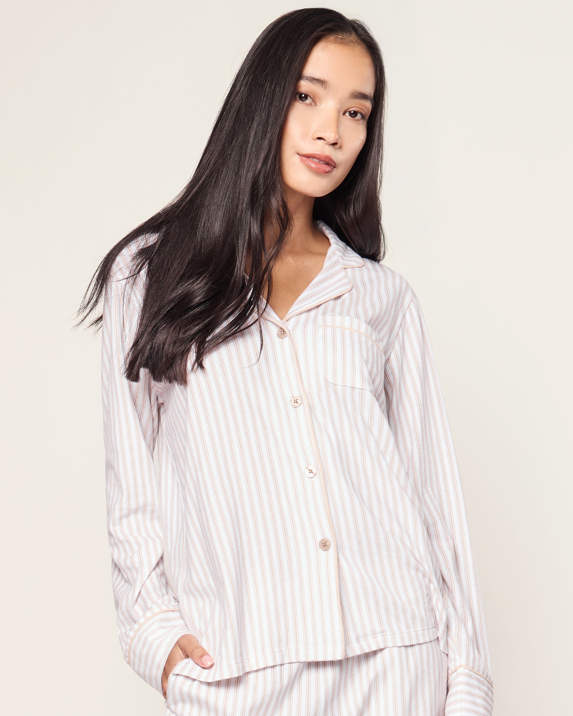 The Women's Pima Pajama Set in Camel Ticking features beige and white vertical stripes, including a long-sleeve button-up top with a chest pocket and matching elastic-waist pants, shown laid flat on a white background.