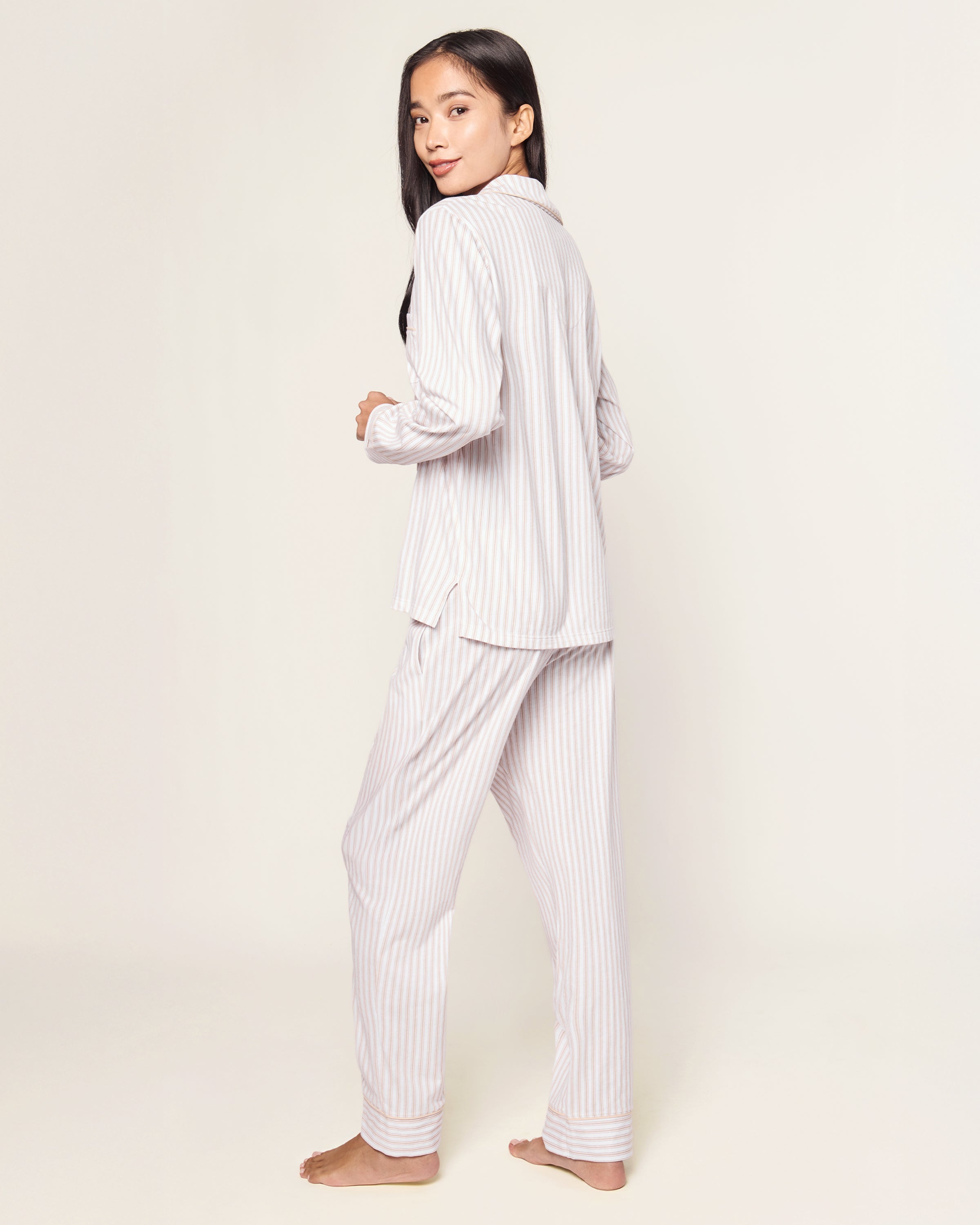 The Women's Pima Pajama Set in Camel Ticking features beige and white vertical stripes, including a long-sleeve button-up top with a chest pocket and matching elastic-waist pants, shown laid flat on a white background.