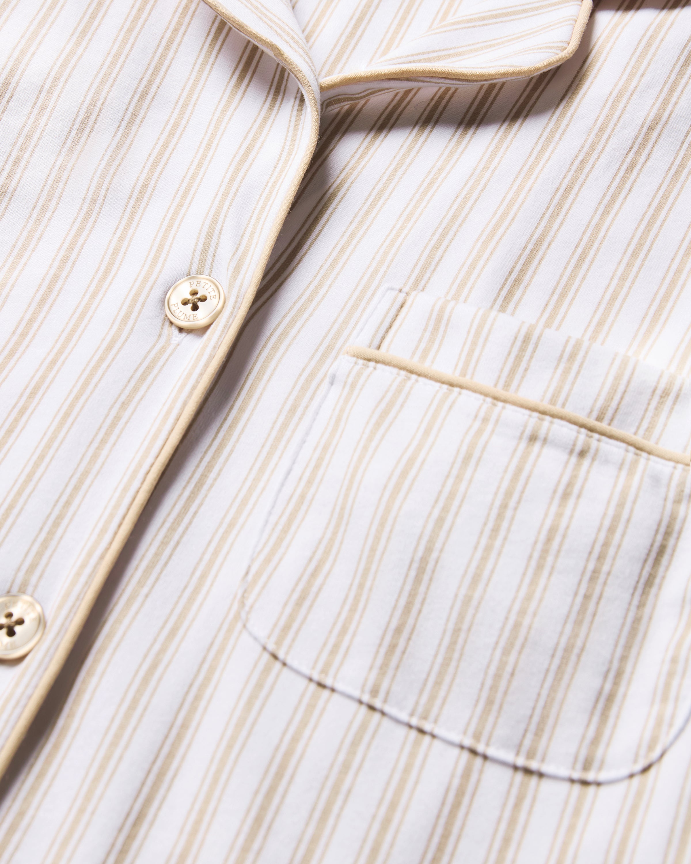 The Women's Pima Pajama Set in Camel Ticking features beige and white vertical stripes, including a long-sleeve button-up top with a chest pocket and matching elastic-waist pants, shown laid flat on a white background.