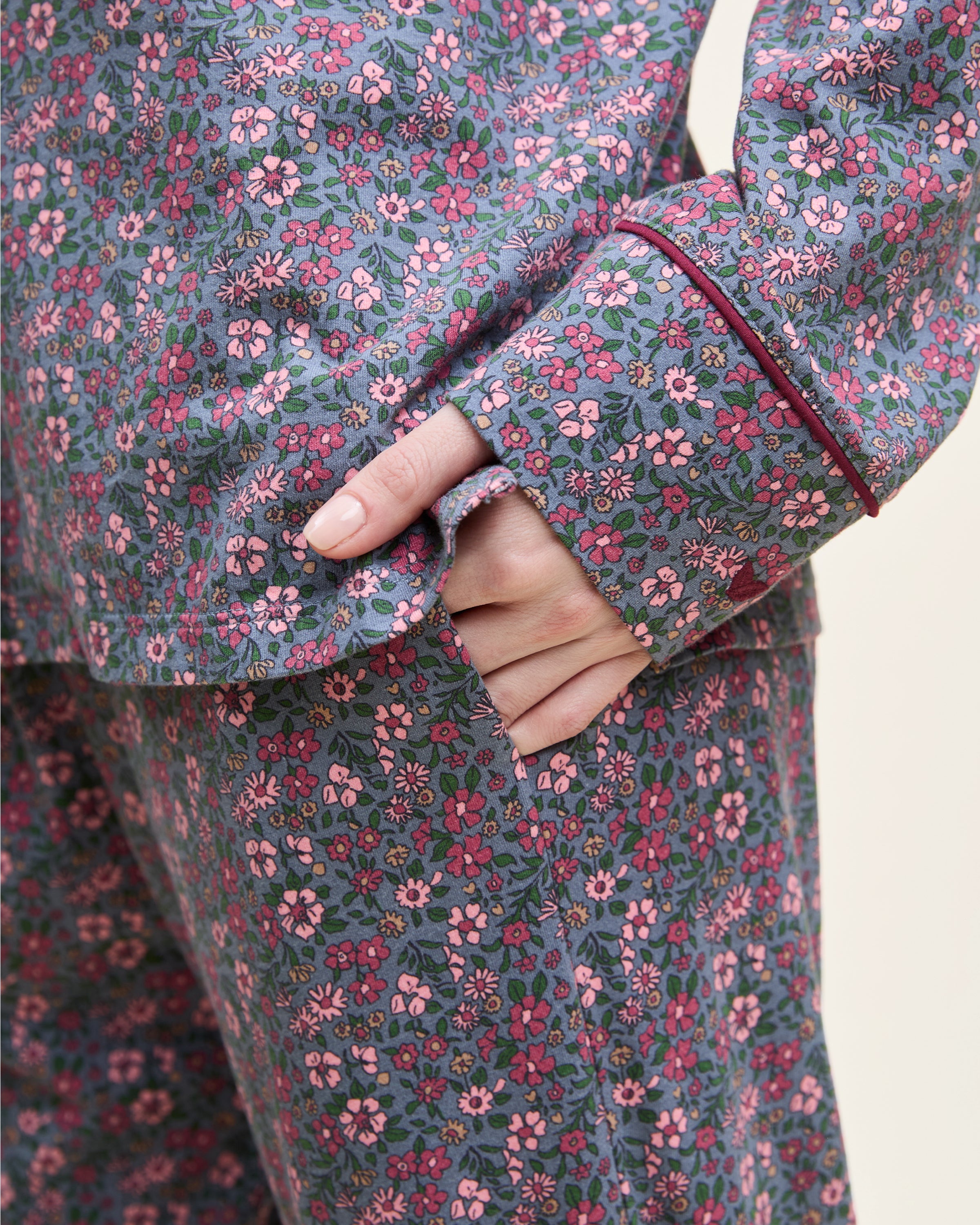 The Women's Pima Pajama Set in Fleurs de Saison features long sleeves and a small floral print in pink, white, and blue on gray. The set includes a button-up top with a chest pocket and matching pants.