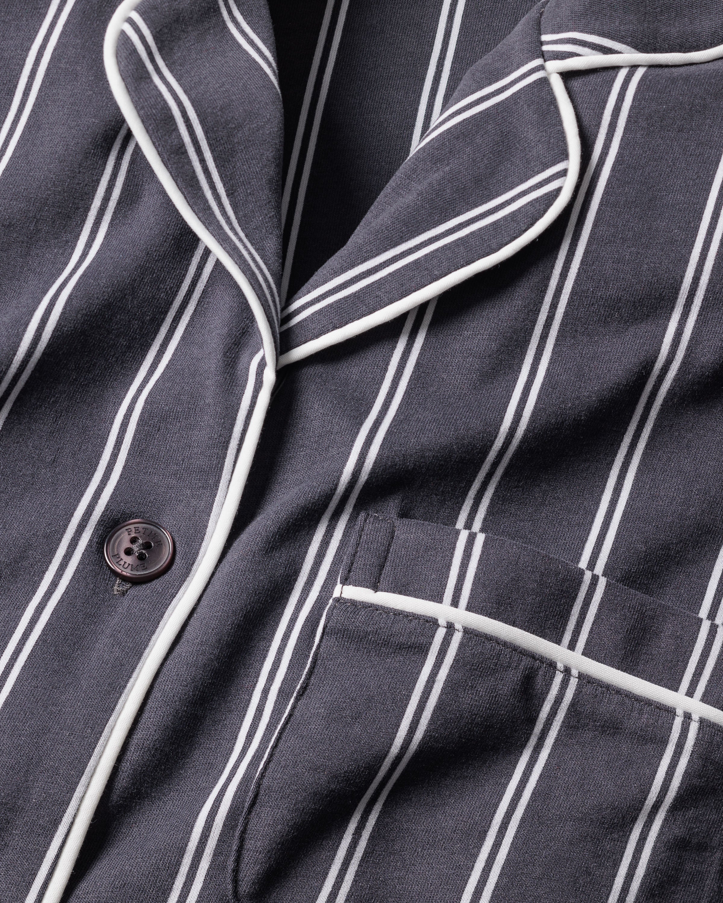 A close-up shows a navy fabric with white stripes, a button, and piped pocket. This likely Pima cotton embodies the elegance of luxury sleepwear, hinting at the Womens Pima Pajama Set in Grey Stripe by Petite Plume.