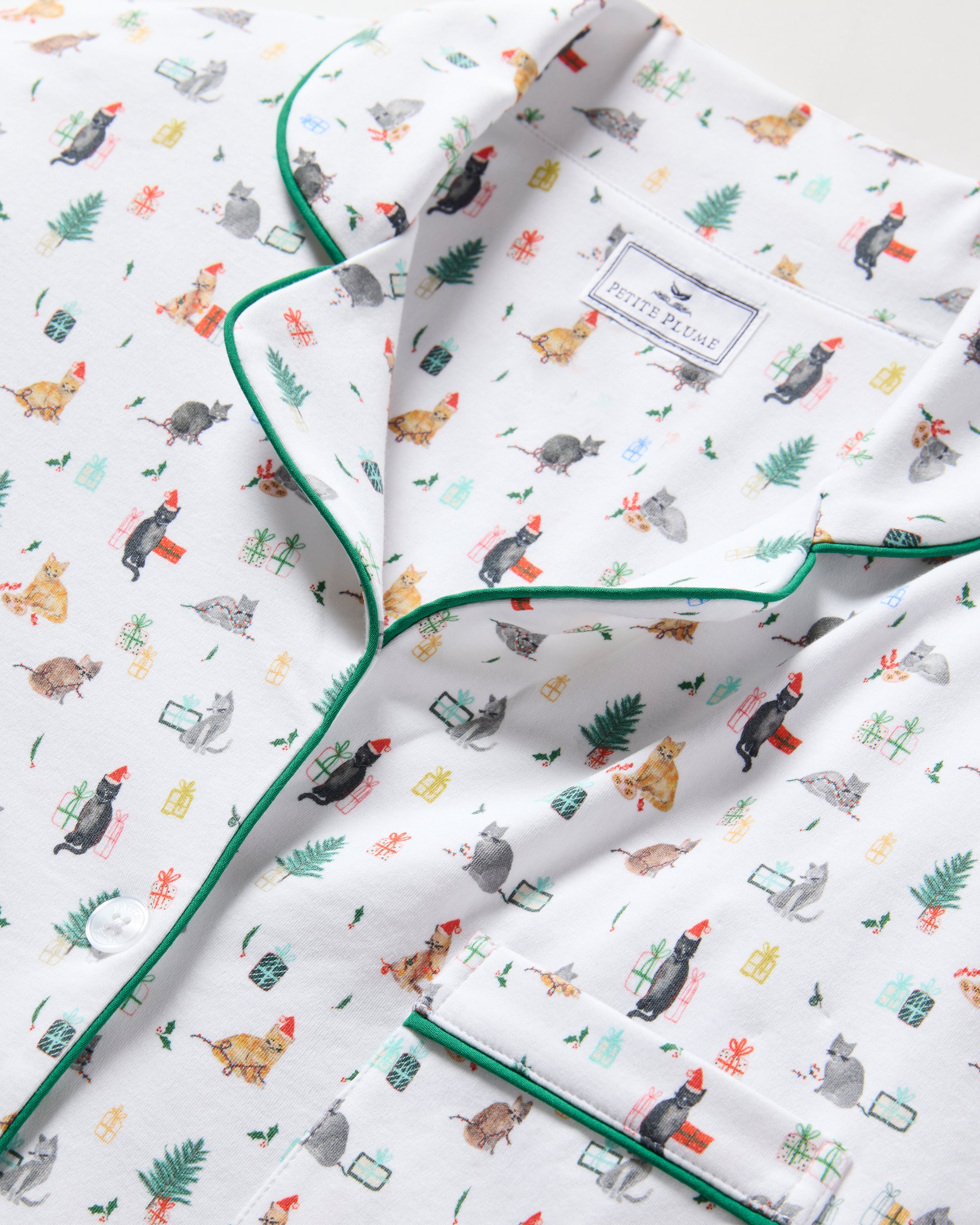 The Women's Pima Pajama Set in Merry Meow features a white, green-piped pajama set with a colorful cat print. Includes a long-sleeve button-up top with chest pocket and matching pants.