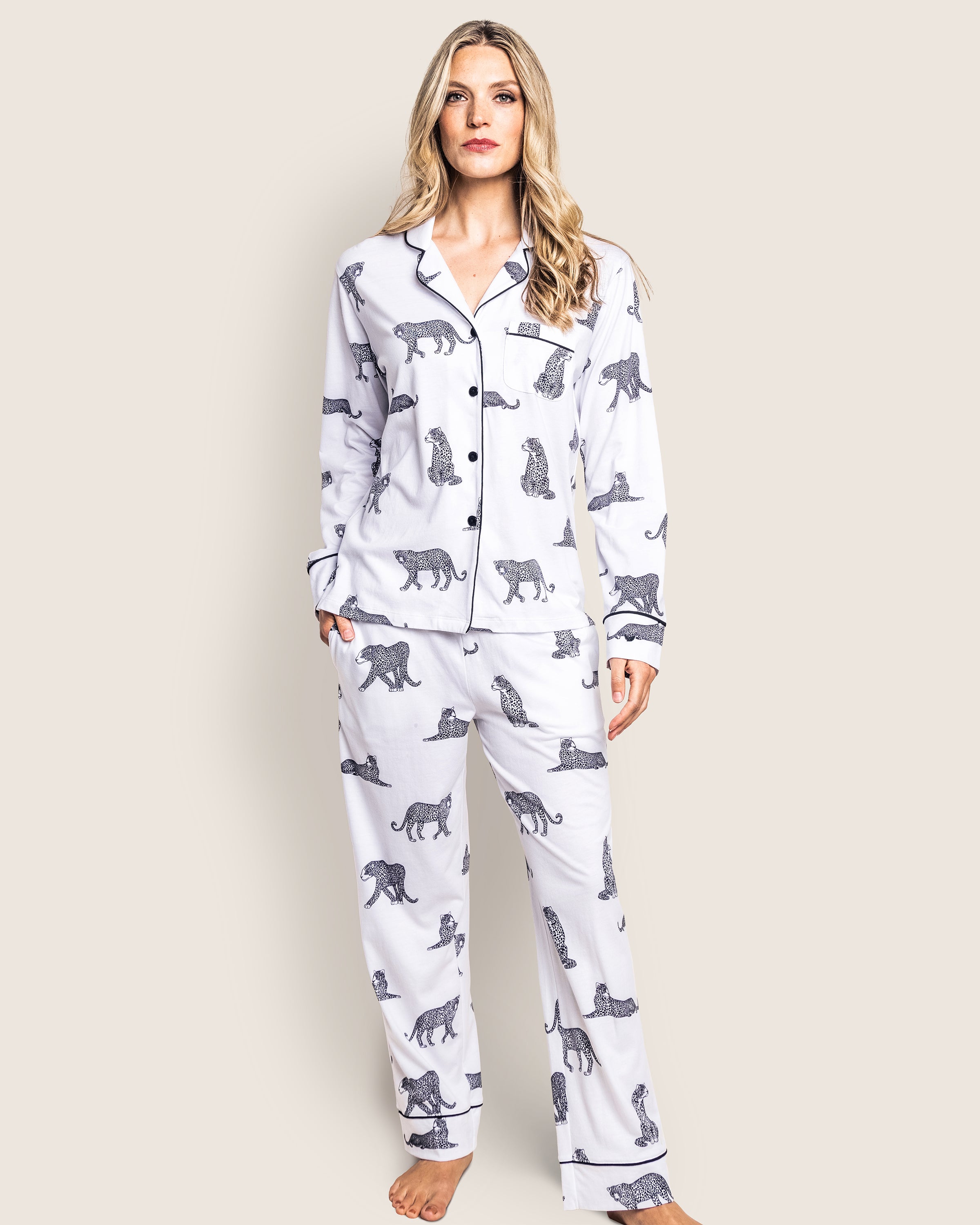 A person stands barefoot in a Womens Pima Pajama Set by Petite Plume. This matching Panthère de Paris set features luxurious Pima cotton, a relaxed fit, and a neutral backdrop with elegant black animal prints. The pajama top includes a collar and buttons for added comfort.