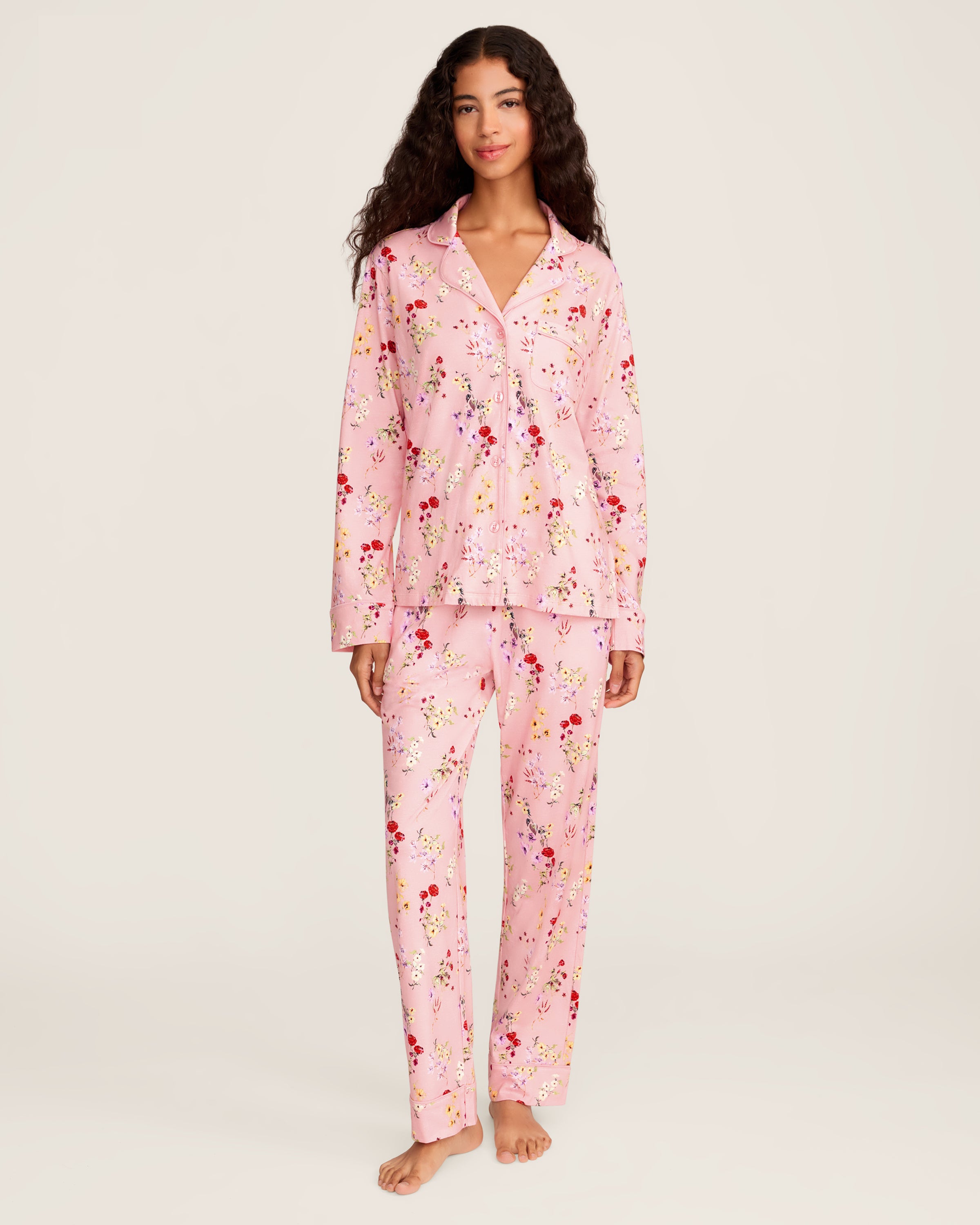 The Women's Pima Pajama Set in Brilliant Botanical Blush features a pink button-up long-sleeve top and matching pants, both adorned with a vibrant floral print in red, white, and purple.
