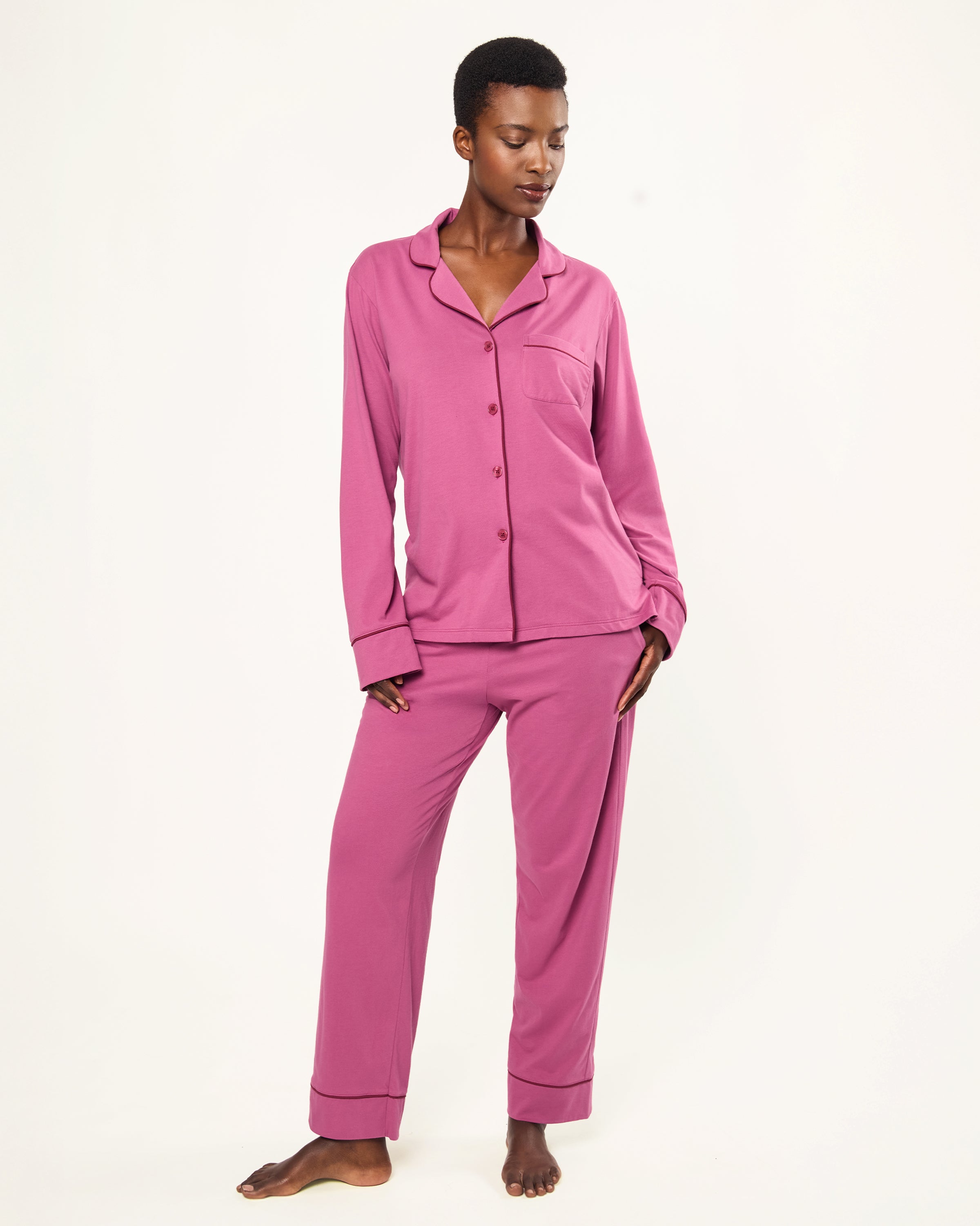 The Women's Pima Pajama Set in Rosewood, featuring a long-sleeve button-up top with a collar and chest pocket, and elastic-waist pants, is shown laid flat on a white background.