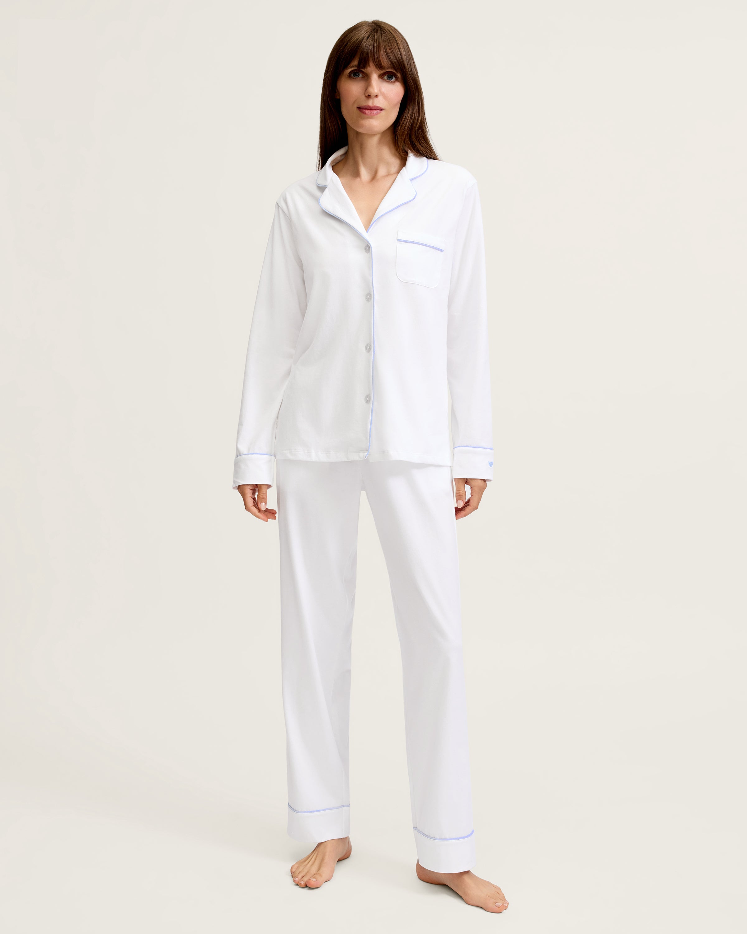 The Women's Pima Pajama Set in White with Periwinkle Piping features a long-sleeve button-up top with a chest pocket and matching pants, both trimmed with periwinkle piping along the collar, cuffs, pocket, and pant hems.