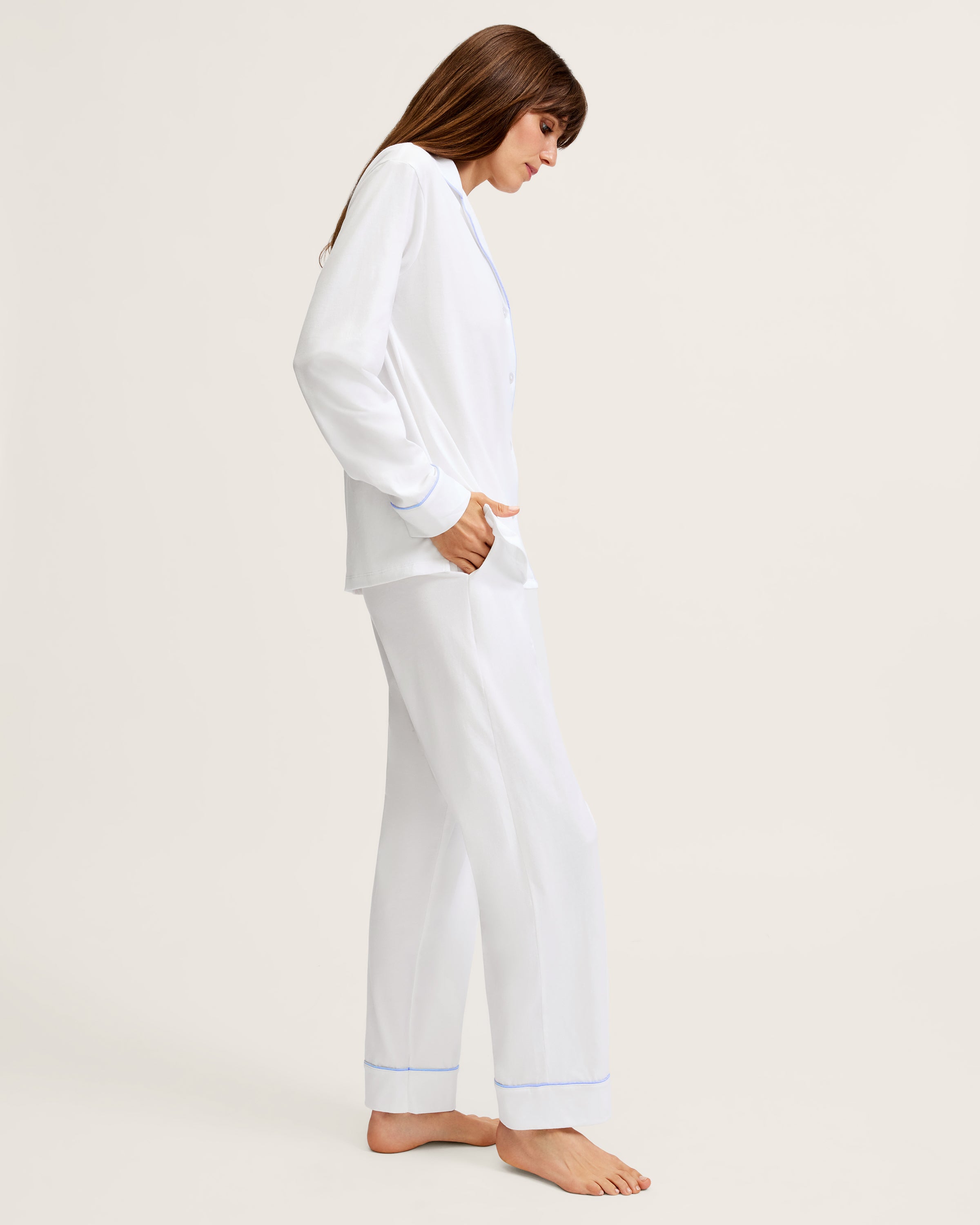 The Women's Pima Pajama Set in White with Periwinkle Piping features a long-sleeve button-up top with a chest pocket and matching pants, both trimmed with periwinkle piping along the collar, cuffs, pocket, and pant hems.