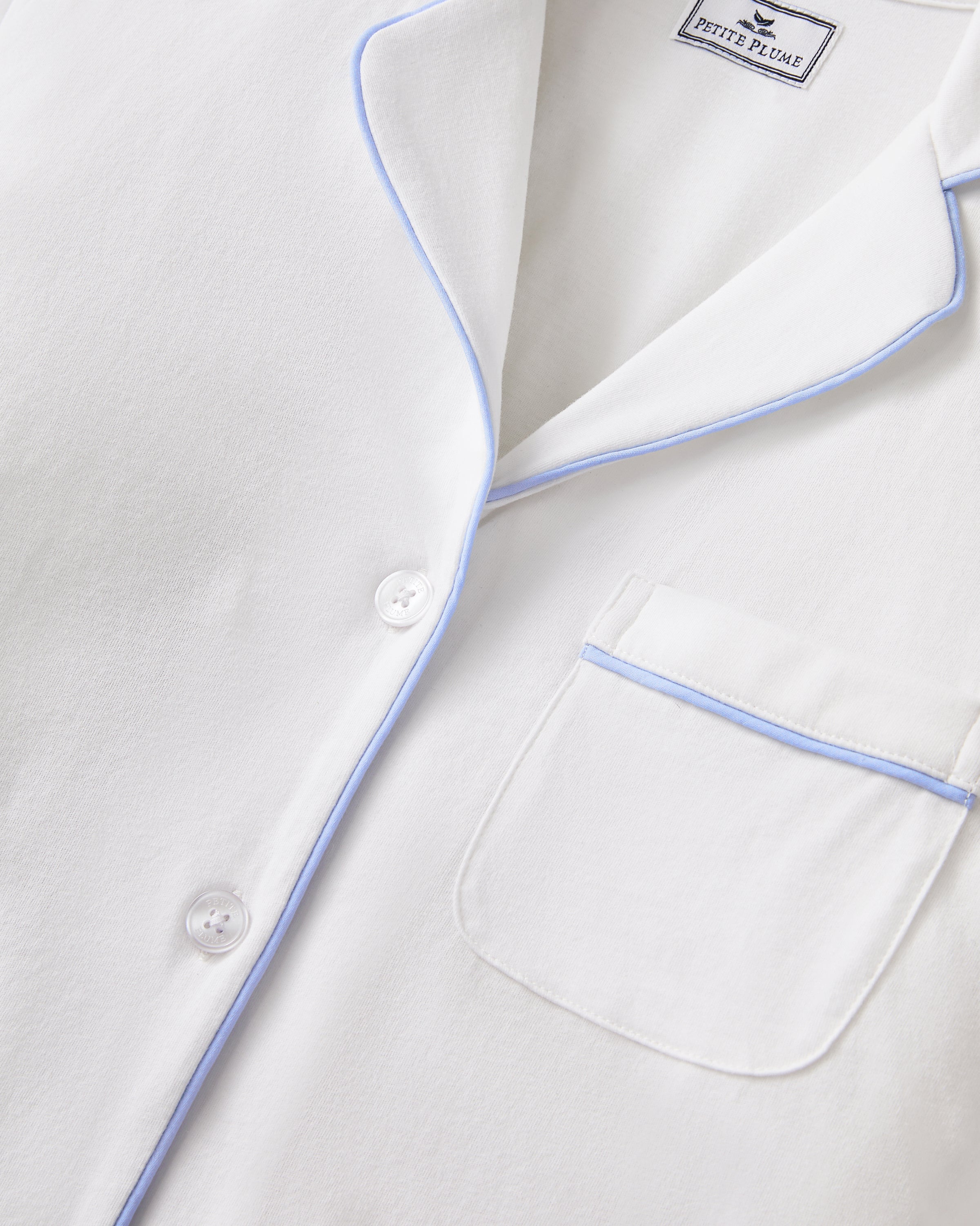 The Women's Pima Pajama Set in White with Periwinkle Piping features a long-sleeve button-up top with a chest pocket and matching pants, both trimmed with periwinkle piping along the collar, cuffs, pocket, and pant hems.