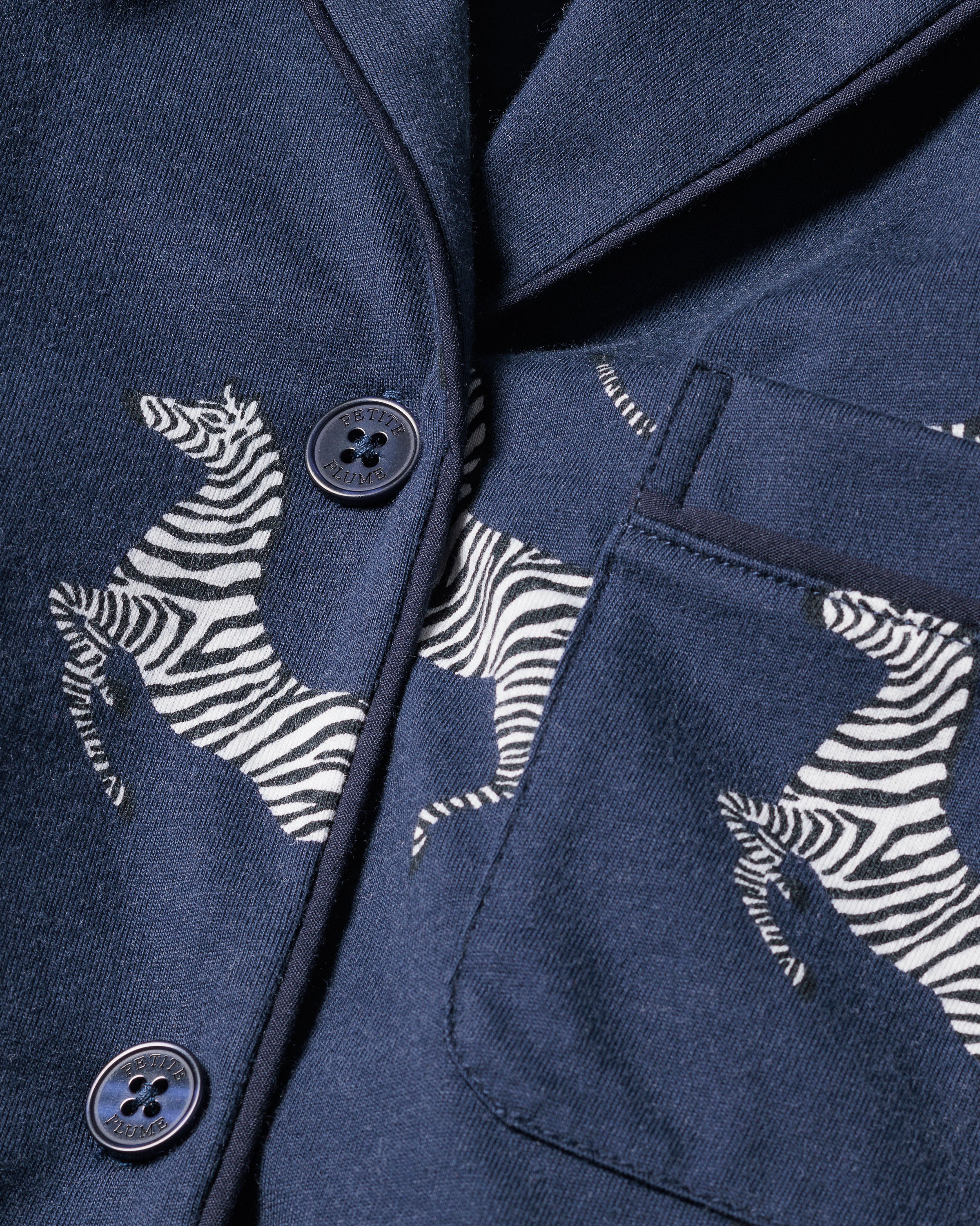 Close-up of Petite Plumes Womens Pima Pajama Set in Zèbre de Nuit, a dark blue ensemble adorned with a zebra print. Crafted from luxurious Peruvian Pima cotton, it showcases exquisite texture with refined details like buttons and a pocket.