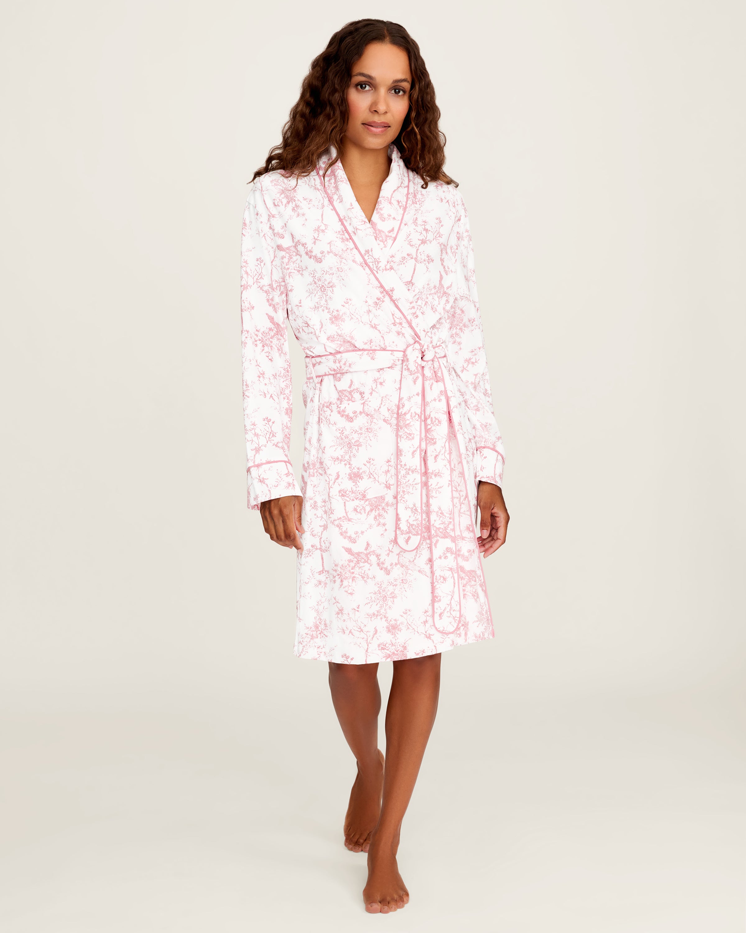 The Women's Pima Robe in Pink Timeless Toile features a white knee-length design with a pink floral toile pattern, long sleeves, a shawl collar, and a matching waist belt.