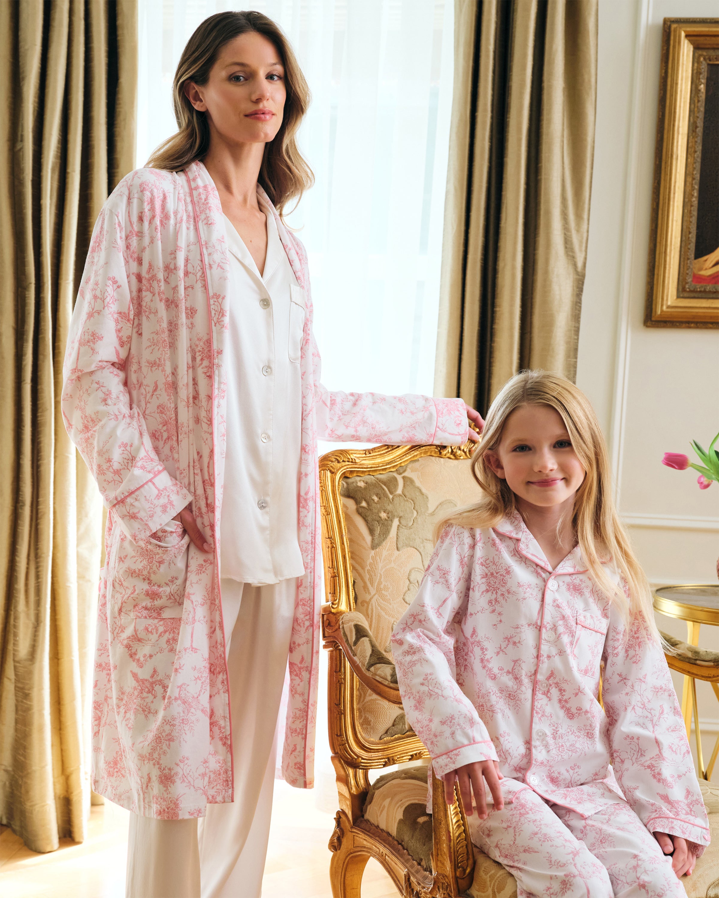 The Women's Pima Robe in Pink Timeless Toile features a white knee-length design with a pink floral toile pattern, long sleeves, a shawl collar, and a matching waist belt.