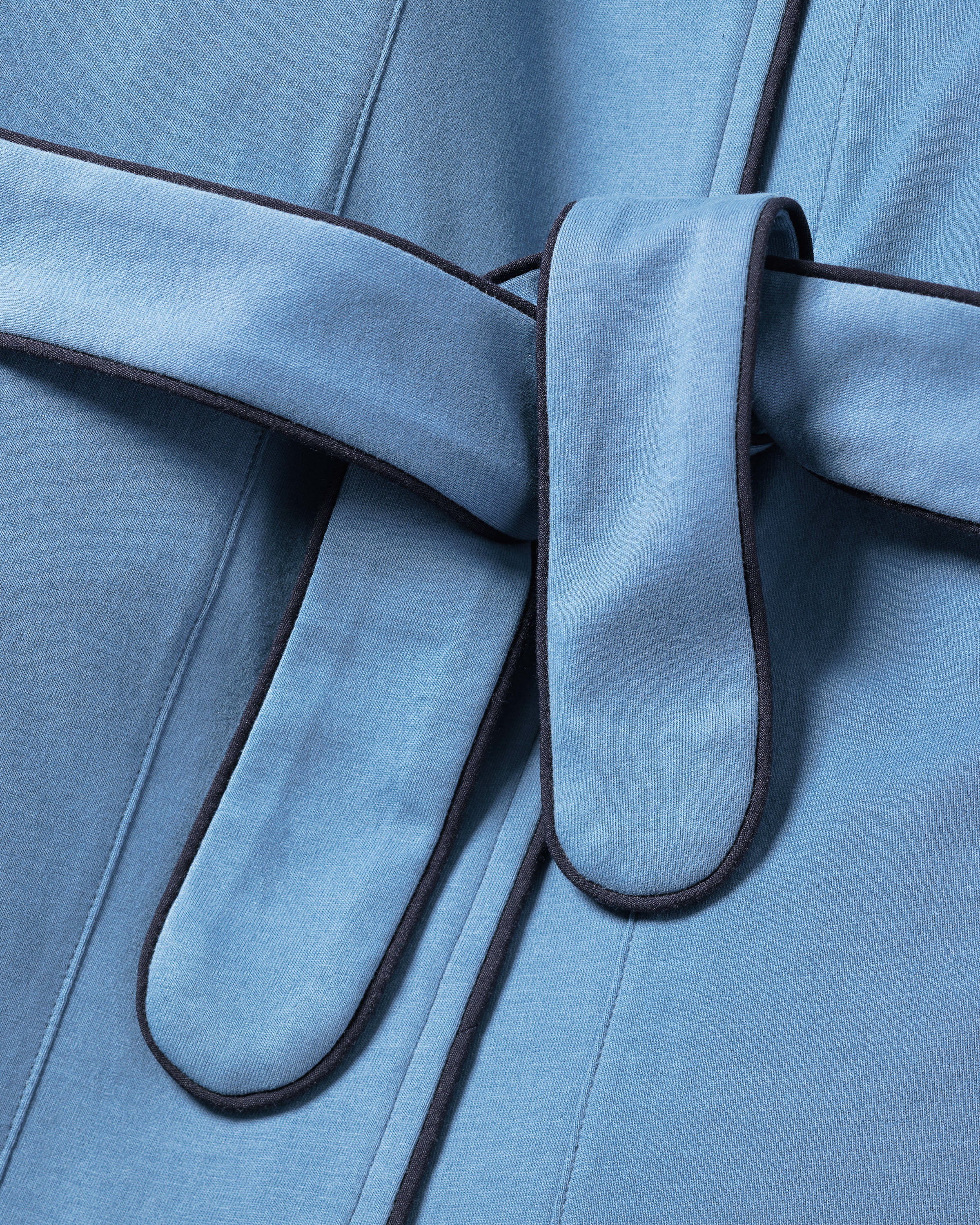 The Womens Pima Robe in Mystique Blue by Petite Plume features fine Pima cotton with dark trim, an elegant belt loop, and a tied belt. Its texture and stitching highlight outstanding craftsmanship, offering luxurious comfort and style for sleepwear.