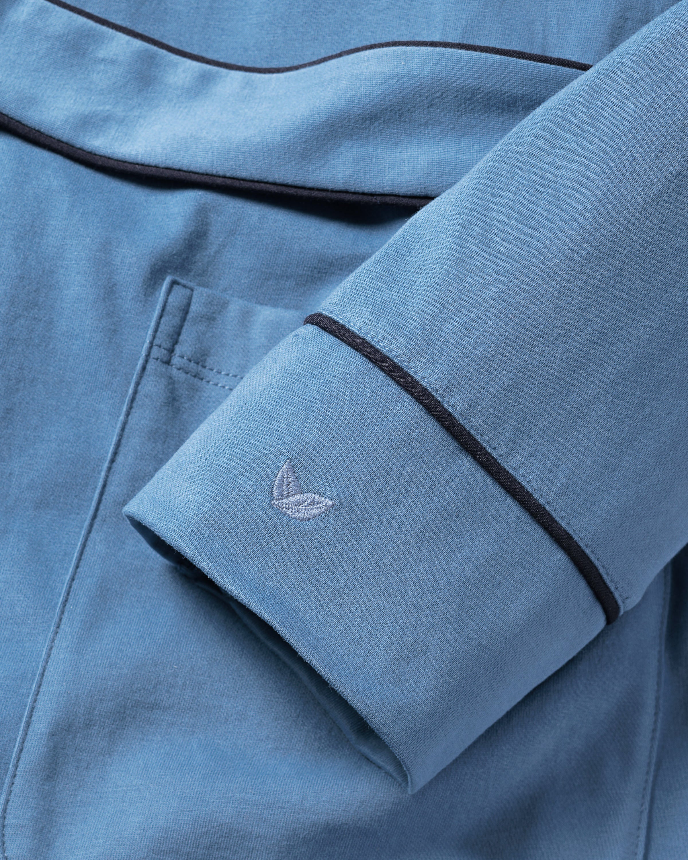 Close-up of the Mystique Blue sleeve from Petite Plumes Womens Pima Robe. It features dark piping along the edges and a subtle embroidered logo near the cuff. The soft Pima cotton fabric exudes luxury sleepwear vibes with a uniform color throughout.
