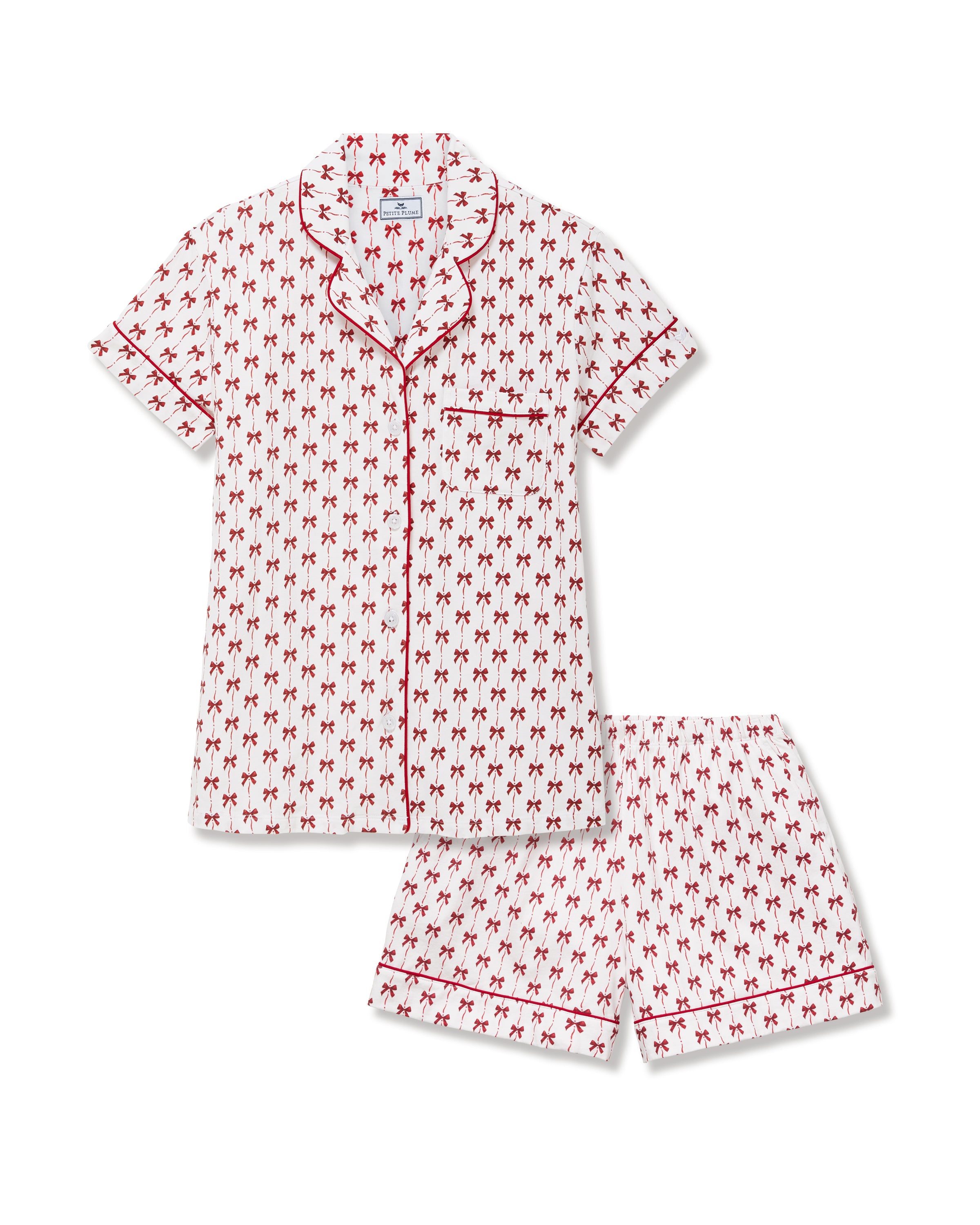 The Women's Pima Short Set in Blissful Bows features a short-sleeve white pajama top and shorts, adorned with a red palm tree pattern and red piping on the edges, collar, pocket, and cuffs.