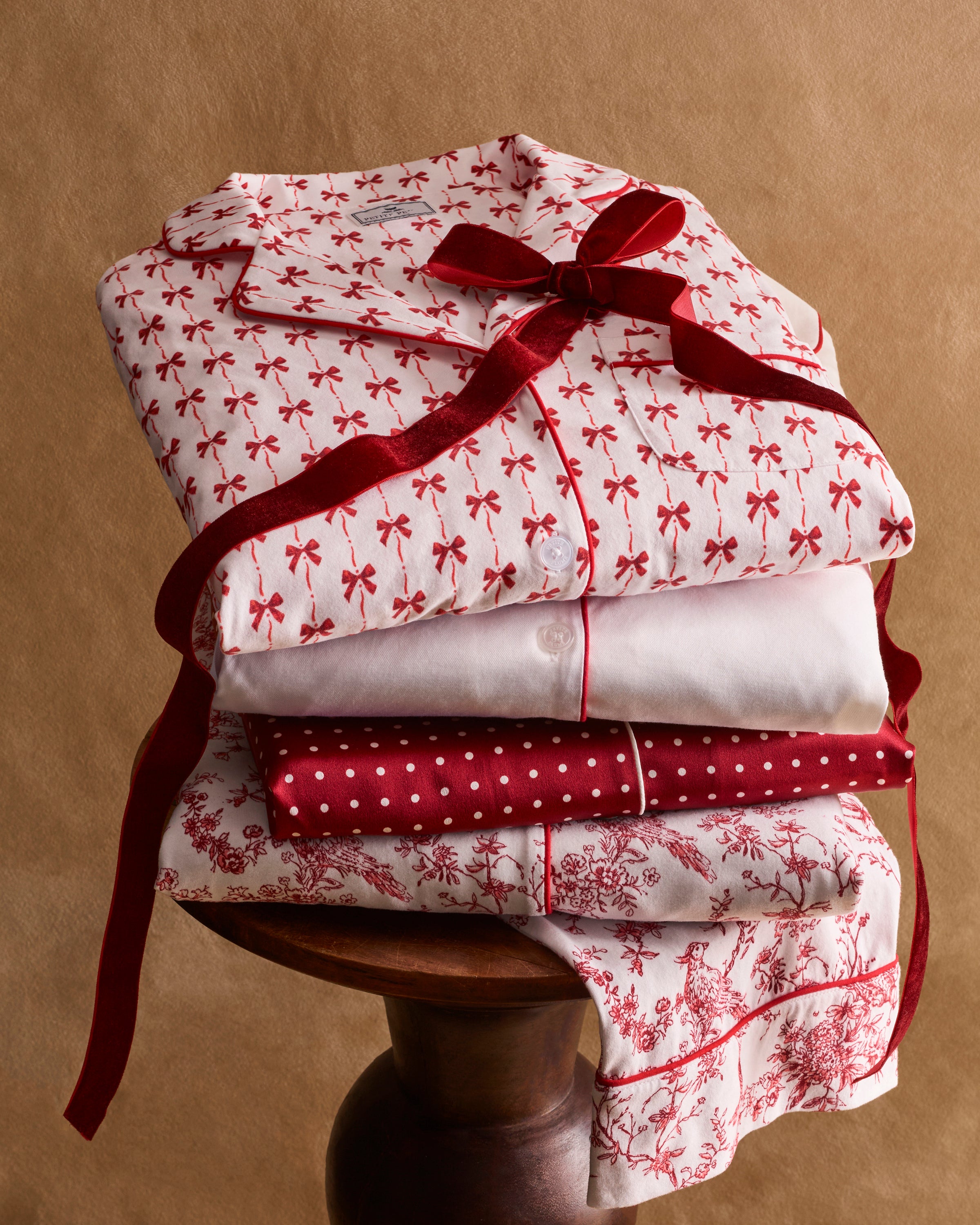 The Women's Pima Short Set in Blissful Bows features a short-sleeve white pajama top and shorts, adorned with a red palm tree pattern and red piping on the edges, collar, pocket, and cuffs.