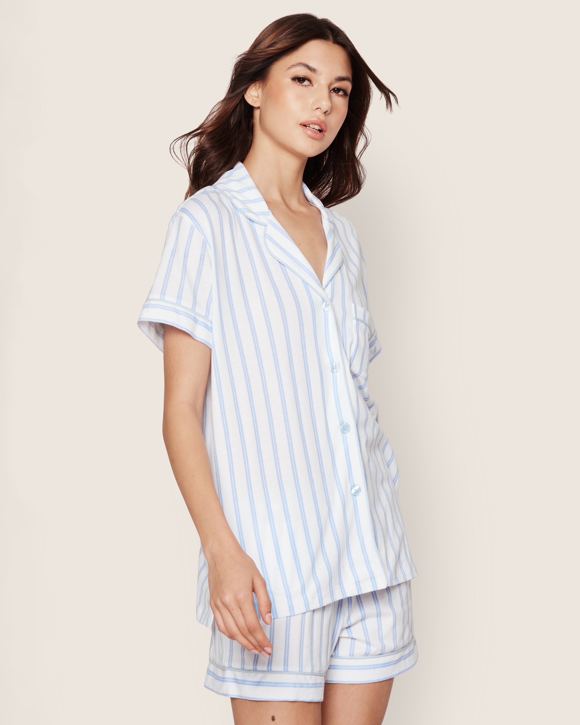 A woman wears Petite Plumes Womens Pima Pajama Short Set in Periwinkle and White Stripe, featuring a soft Pima cotton short-sleeve button-up top and shorts, against a plain light background.