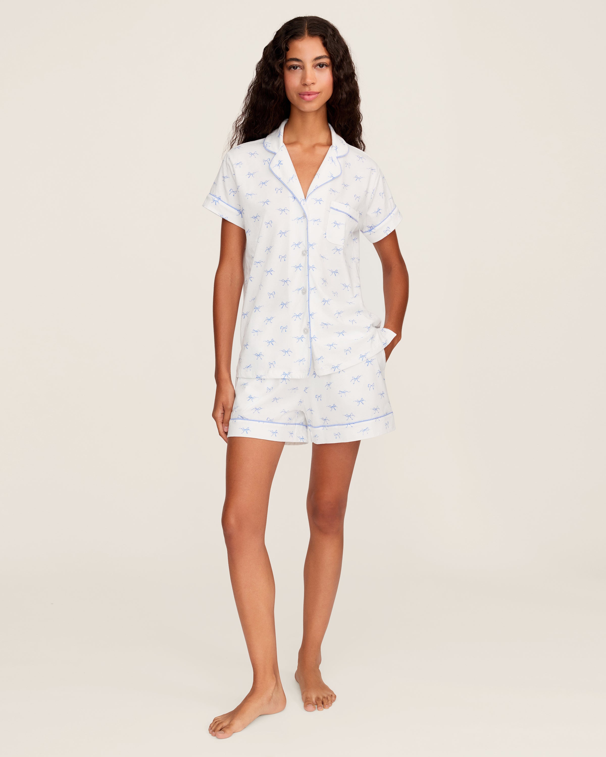 Women's Pima Short Sleeve Short Set in Something Blue Bows features a collared button-up top with chest pocket and matching elastic-waist shorts, both adorned with all-over blue bow print and contrast piping.