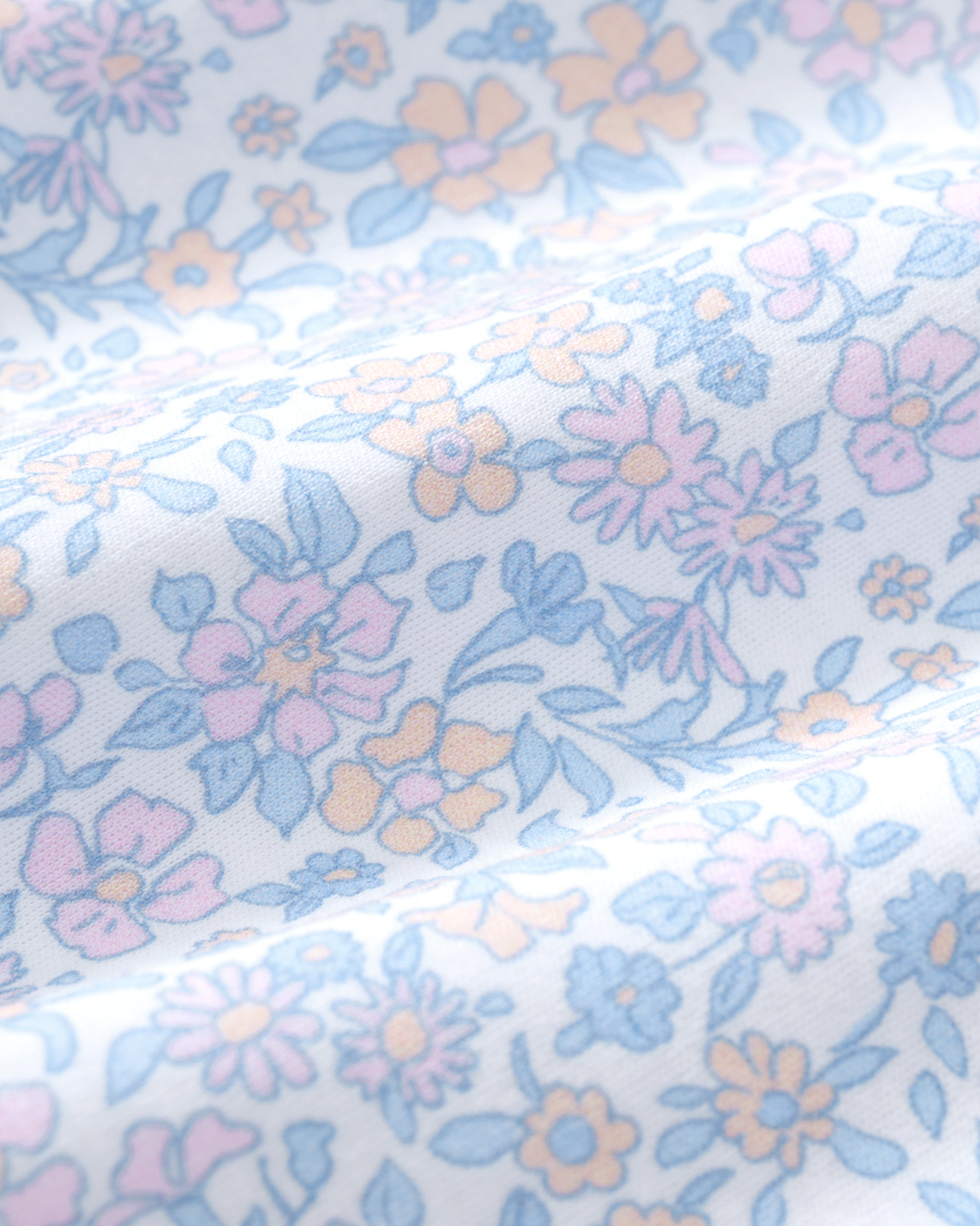 A woman with long wavy hair wears the Women's Lightweight Pima Short Sleeve Short Set in Fleur Blanche, featuring a pastel floral pattern, standing against a plain background.