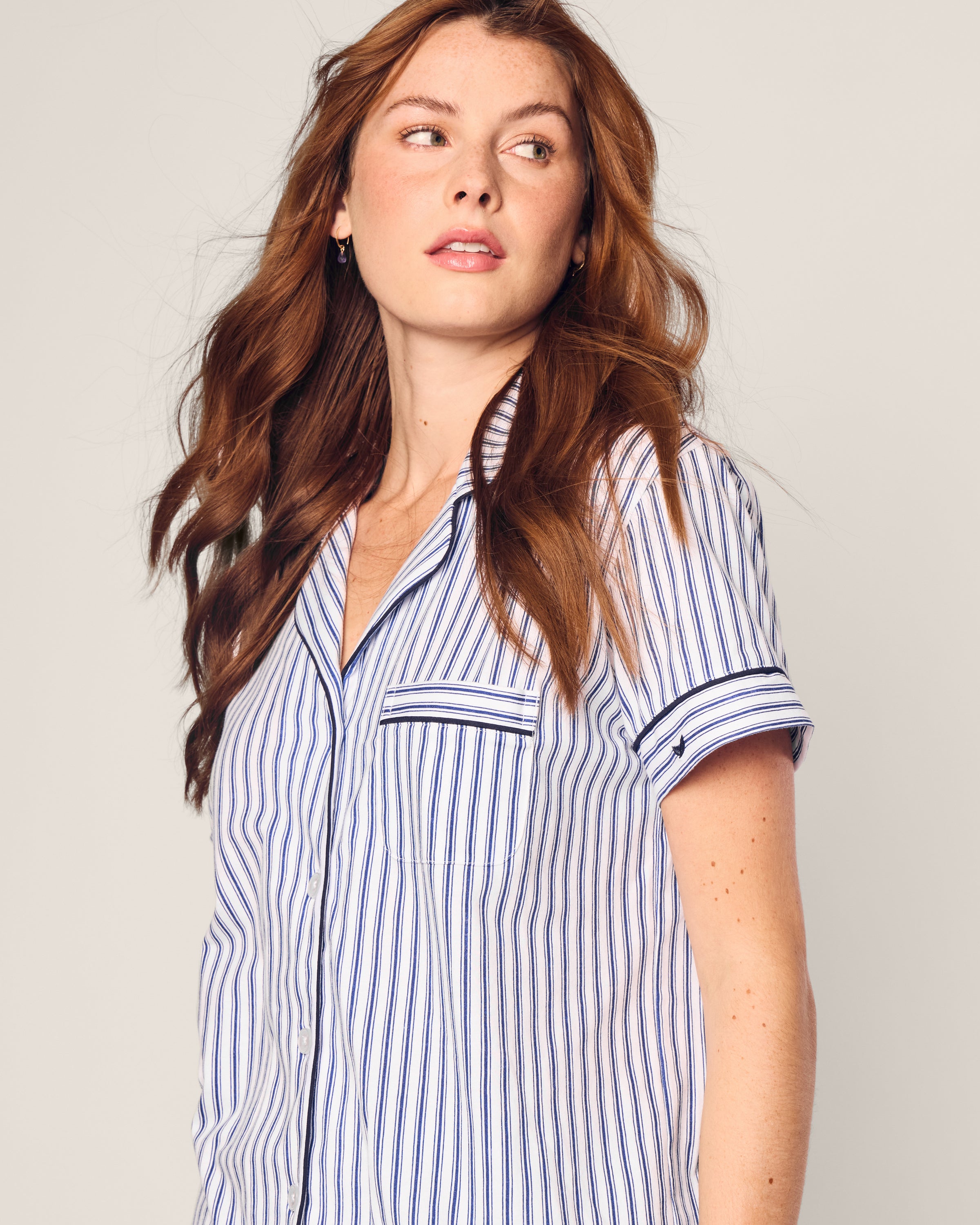 A woman with long, wavy auburn hair wears the Womens Pima Pajama Short Set in Navy French Ticking by Petite Plume. She gazes right with a neutral expression against a plain, light background.