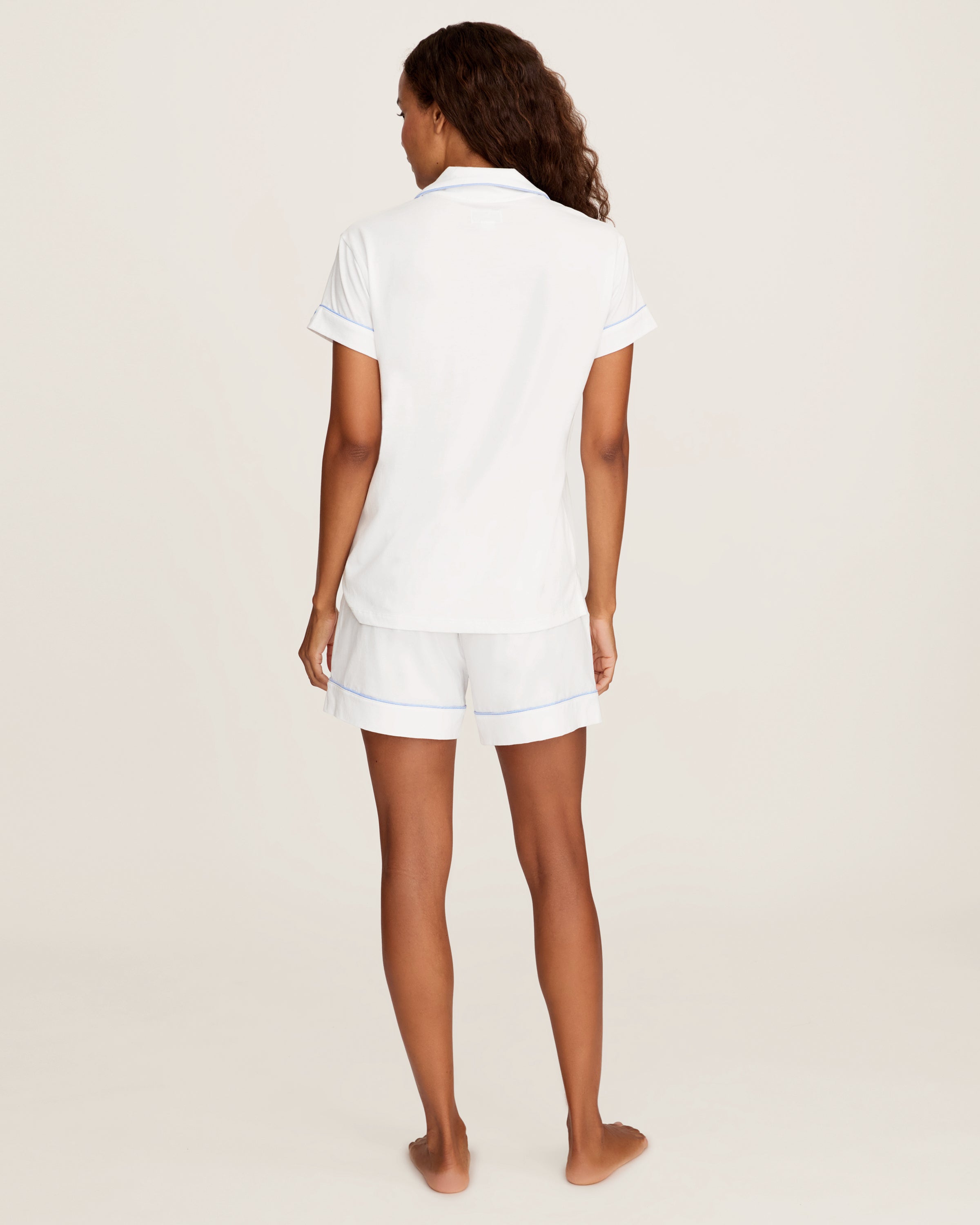 The Women's Pima Short Sleeve Short Set in White with Periwinkle Piping includes a collared button-up top with a chest pocket and matching shorts featuring an elastic waistband.