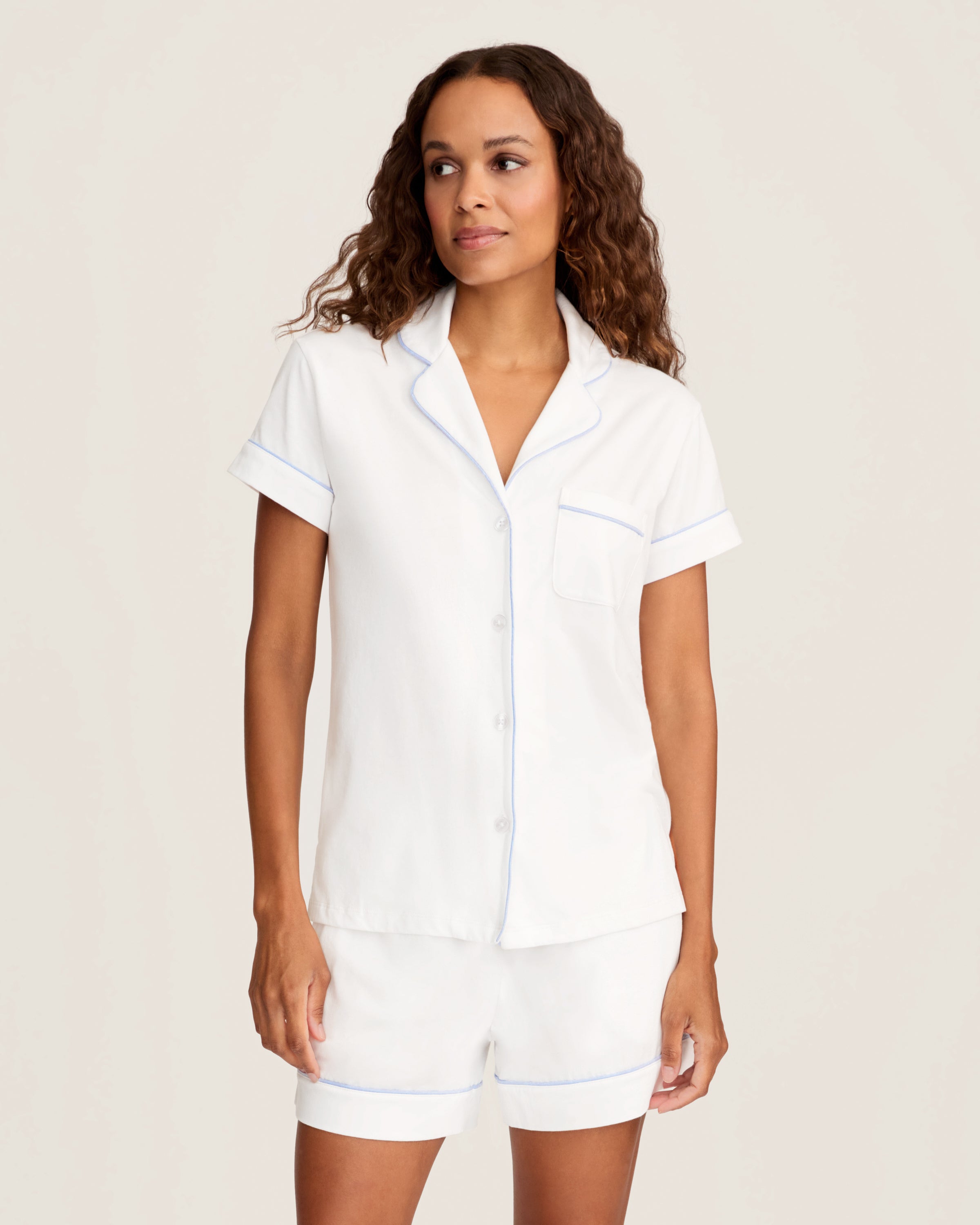 The Women's Pima Short Sleeve Short Set in White with Periwinkle Piping includes a collared button-up top with a chest pocket and matching shorts featuring an elastic waistband.