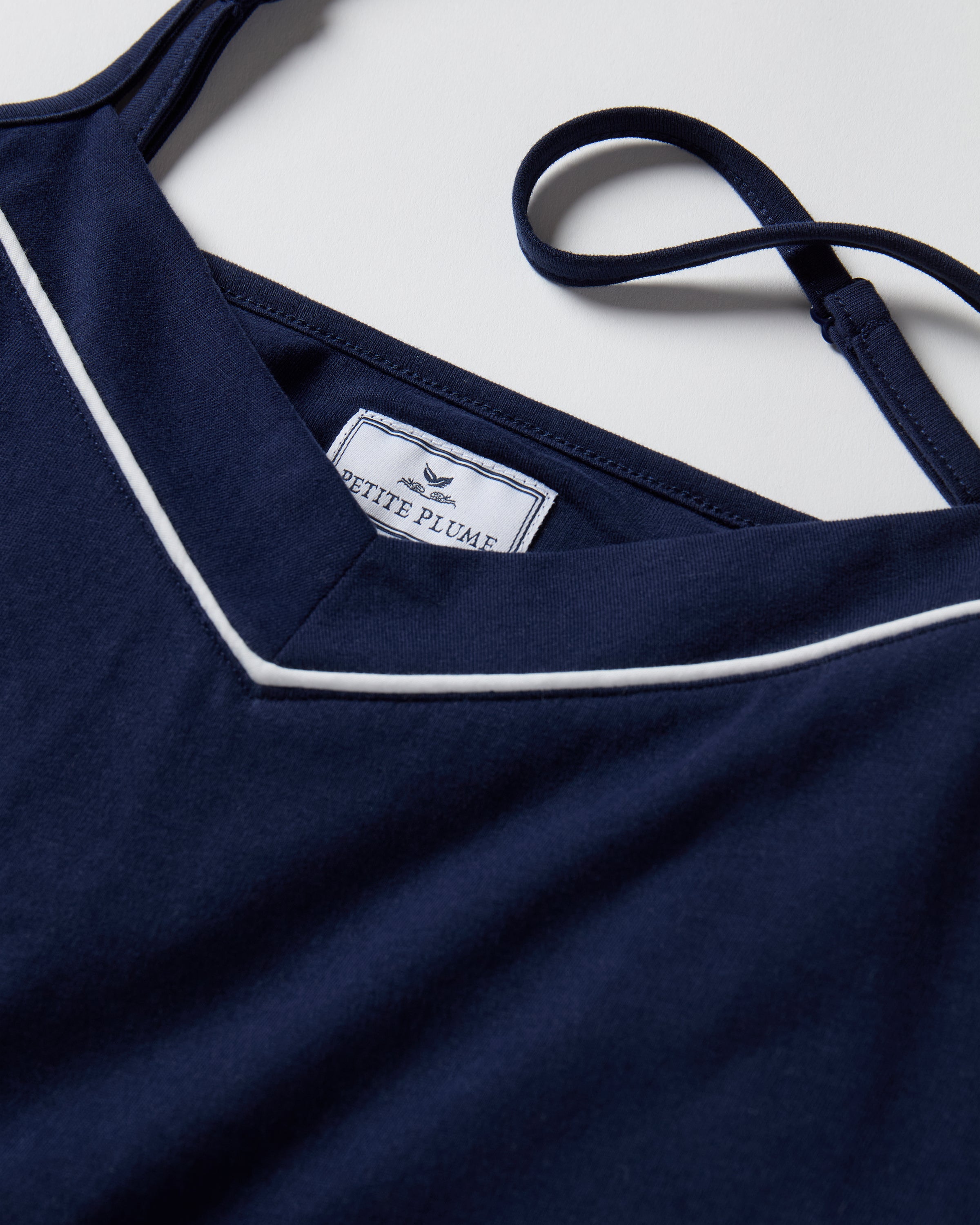 The Women's Pima Sylvie Pajama Set in Navy includes a sleeveless V-neck camisole with thin straps and matching long pants, both featuring white trim. The set is displayed flat on a white background.