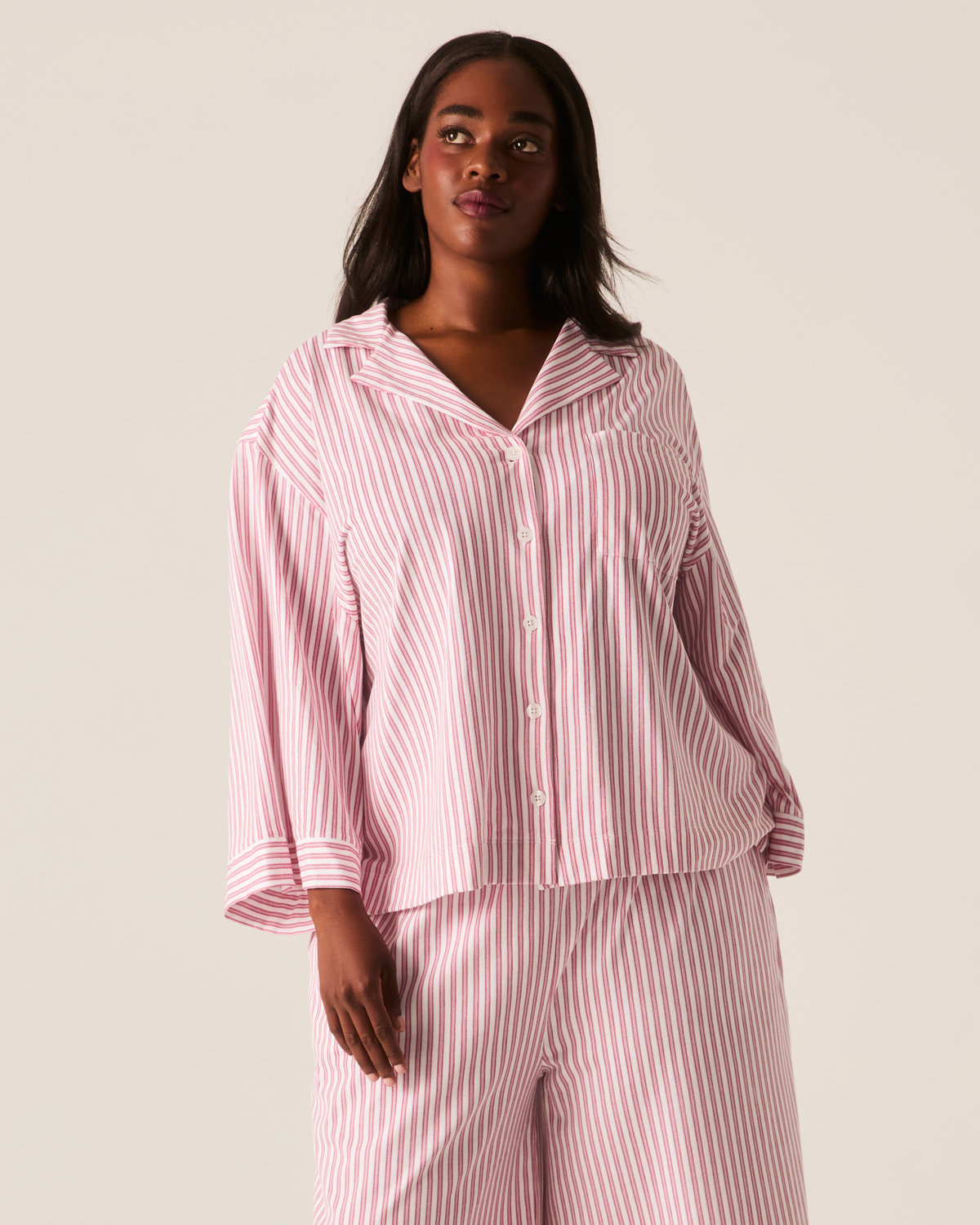 A person wearing The Olivia Wide Leg Pima Pajama Set in Antique Red Ticking, featuring a long-sleeved button-up shirt and wide-leg trousers in a red and white vertical stripe pattern.