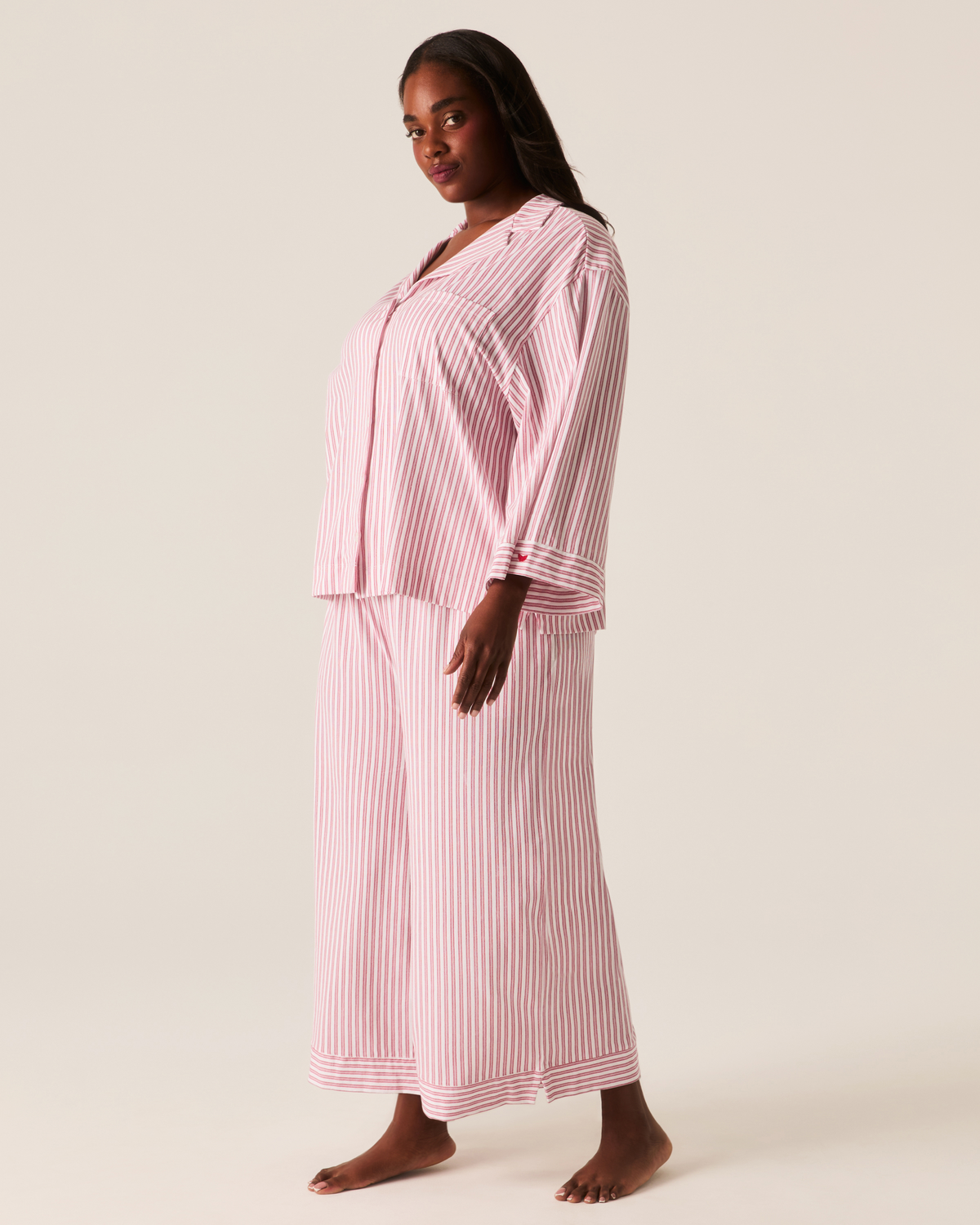 A person wearing The Olivia Wide Leg Pima Pajama Set in Antique Red Ticking, featuring a long-sleeved button-up shirt and wide-leg trousers in a white and red pinstripe pattern.