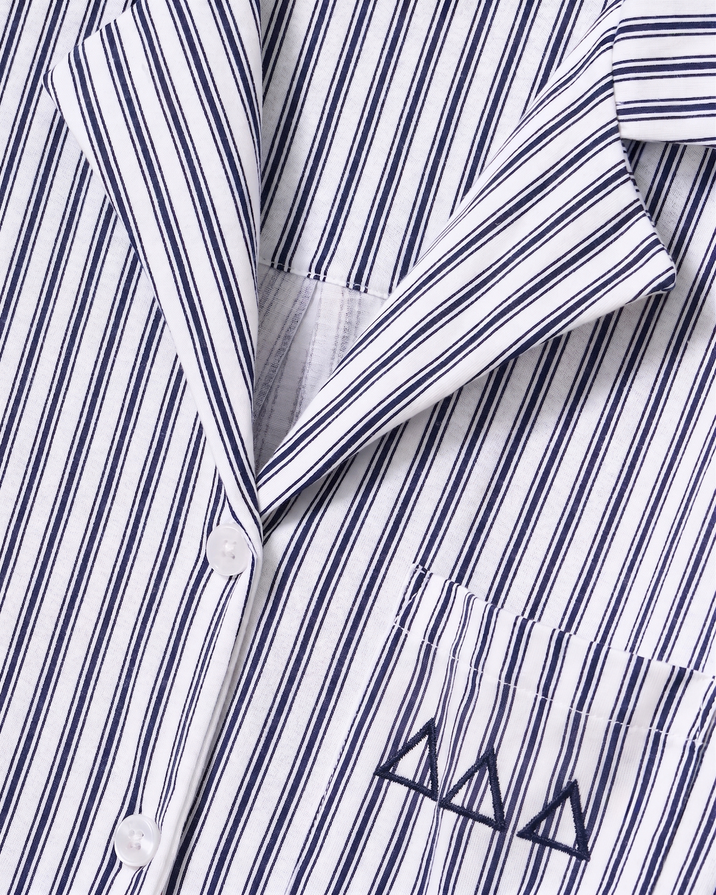 Close-up of the Greek Embroidered Olivia Wide Leg Pima Pajama Set in Navy French Ticking, featuring a white shirt with thin black vertical stripes, white buttons, a pocket, and three black embroidered triangle shapes on the pocket.
