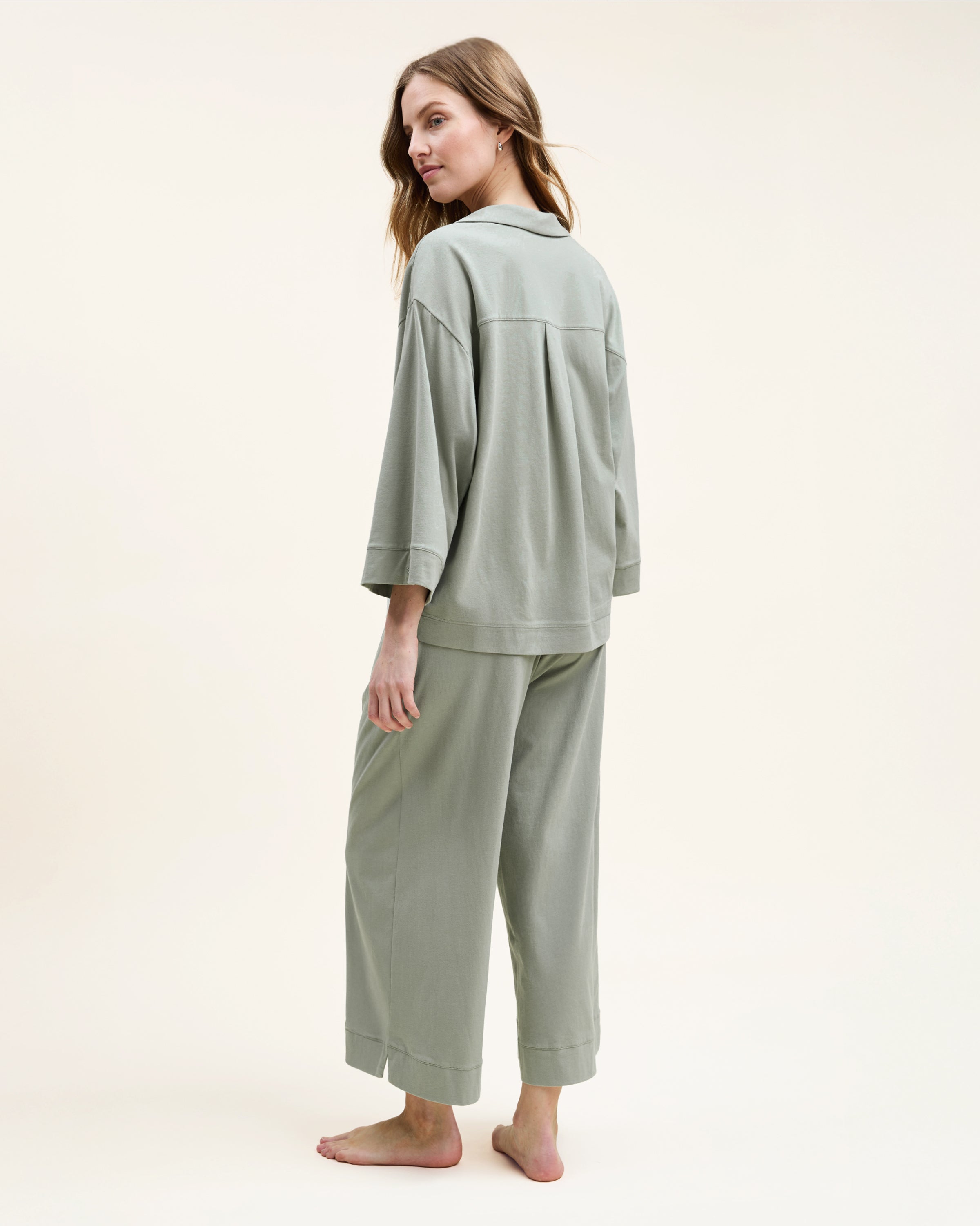 The Olivia Wide Leg Pima Pajama Set in Sage includes a button-up, collared top with a chest pocket and three-quarter sleeves, plus matching elastic waist wide-leg pants. Both pieces are neatly laid flat on a white background.